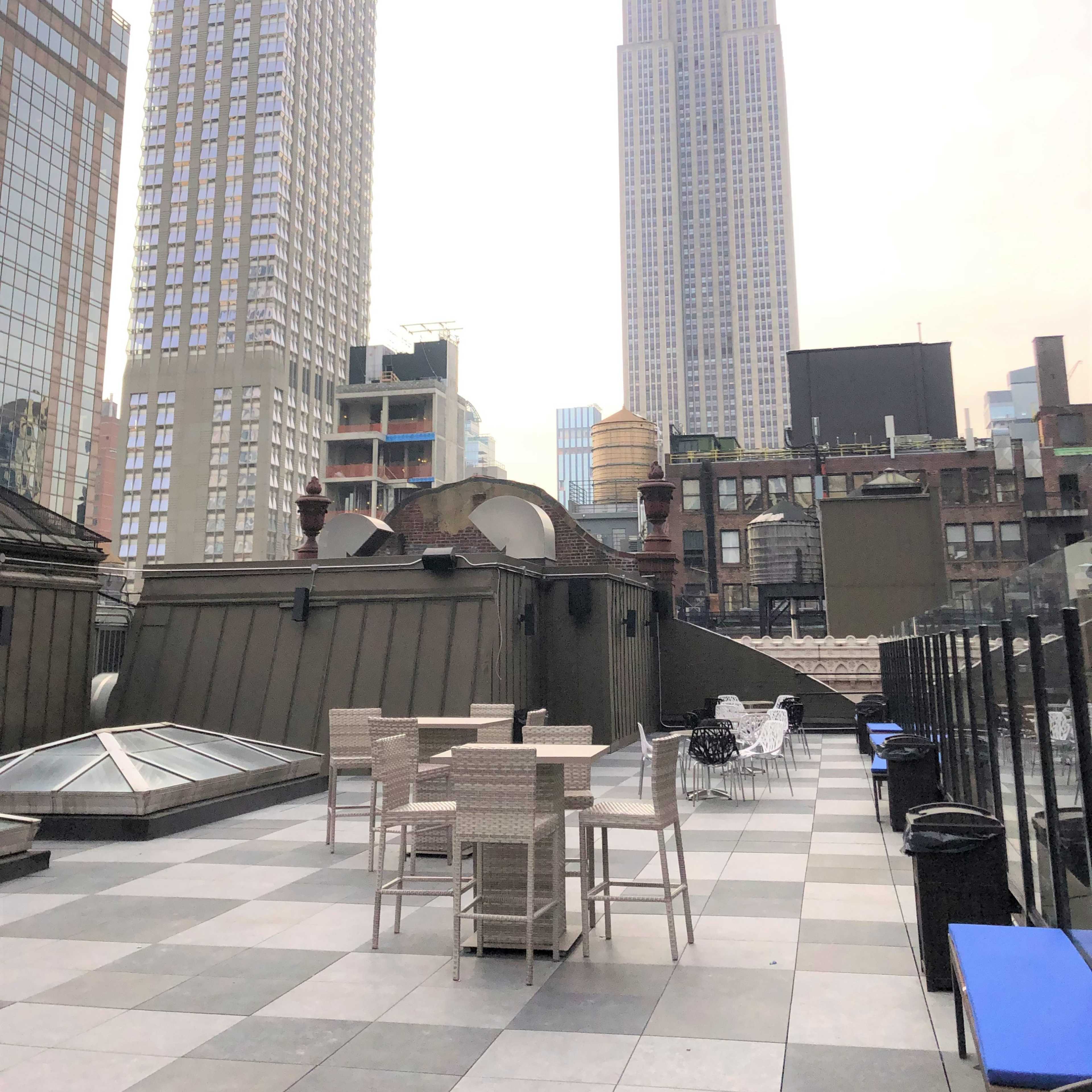 The rooftop terrace features outdoor furniture with the Empire State Building prominently visible in the background.