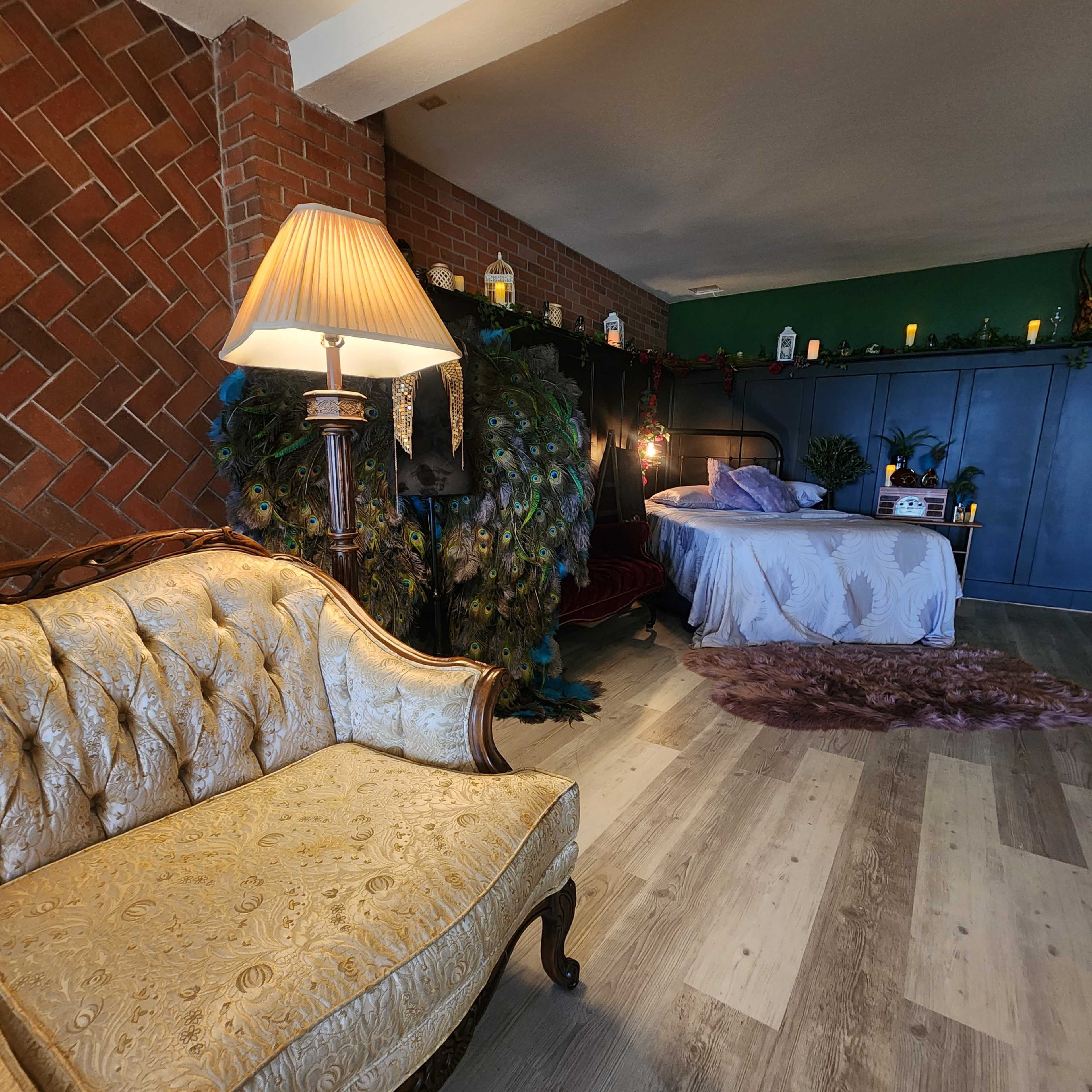 A room with a vintage gold sofa, a peacock-themed decor along the wall, and a bed with a purple cover positioned in a cozy corner.