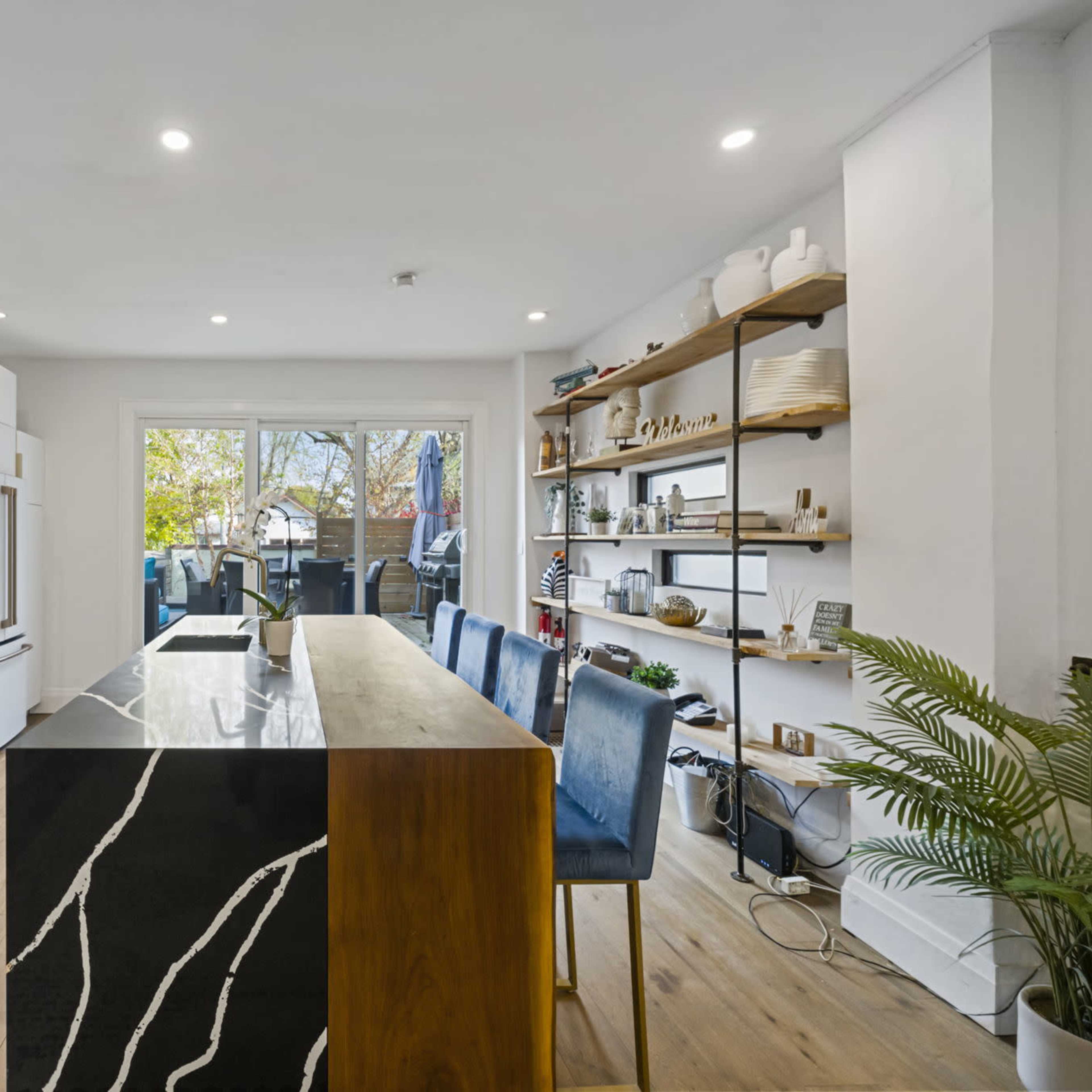 A modern kitchen featuring white cabinets, a black and wood island with bar seating, and open shelving displaying kitchenware.
