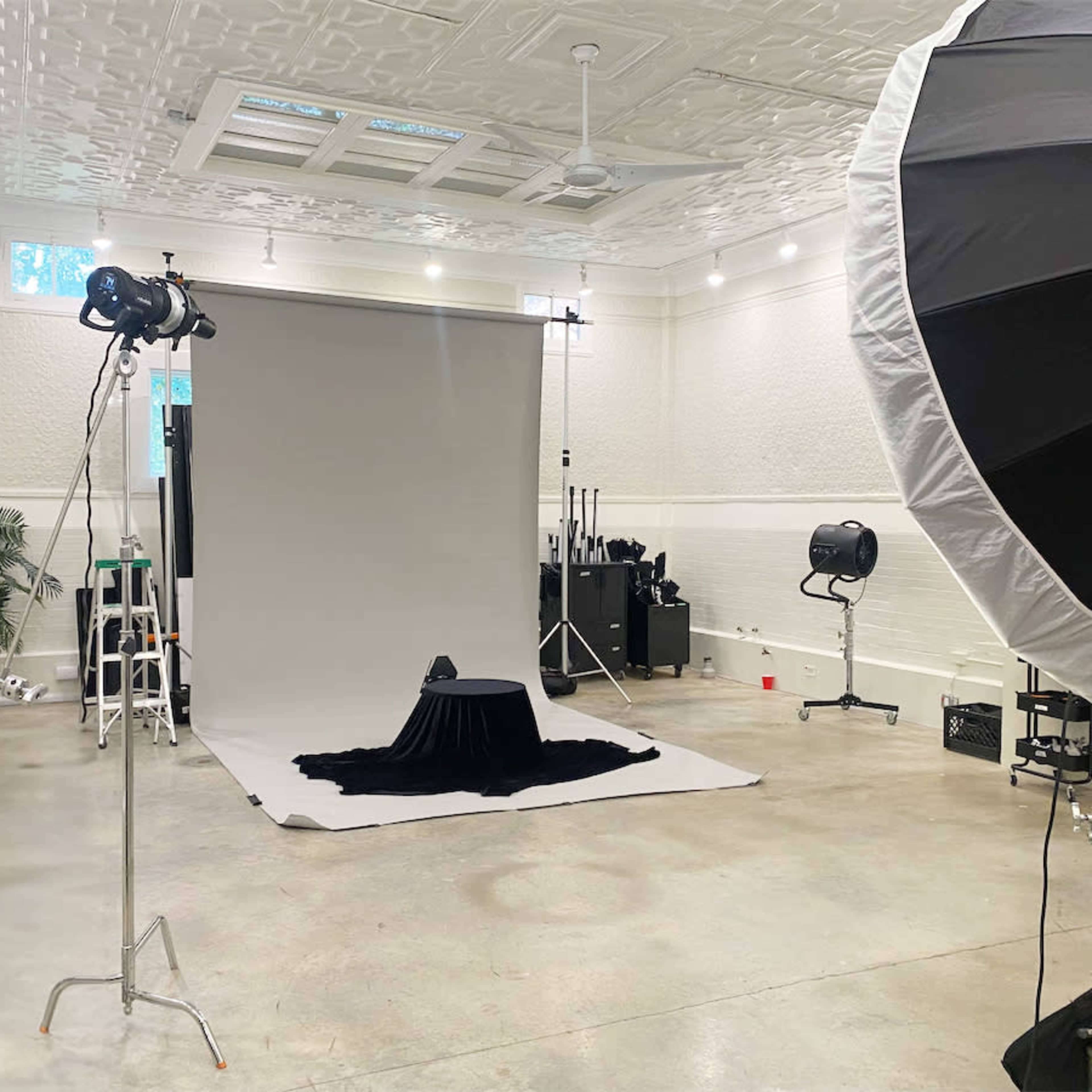 A photography studio with a backdrop, lighting equipment, and a black cloth draped over a small table.