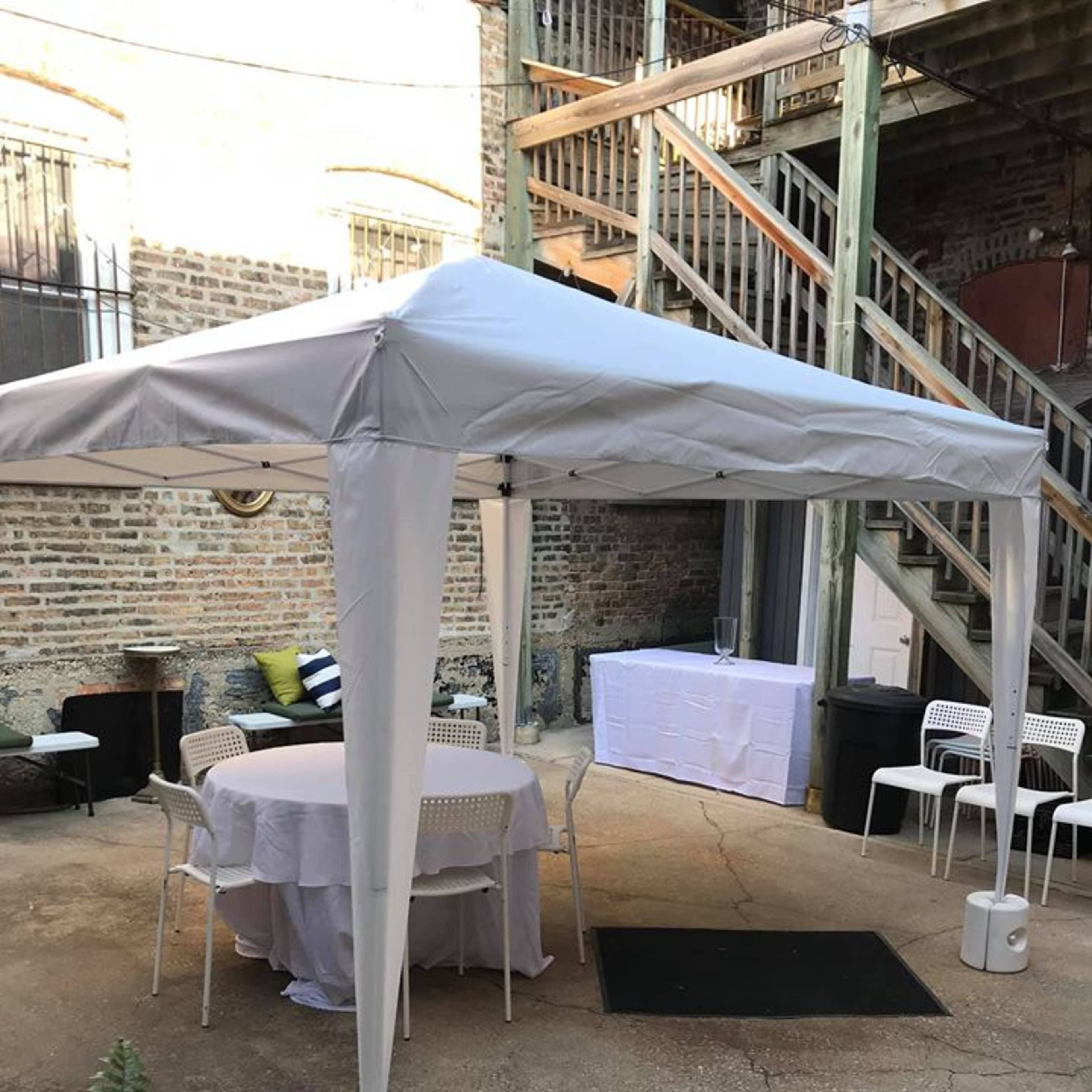 A white tent is set up in a courtyard on a concrete floor, surrounded by chairs and a table.