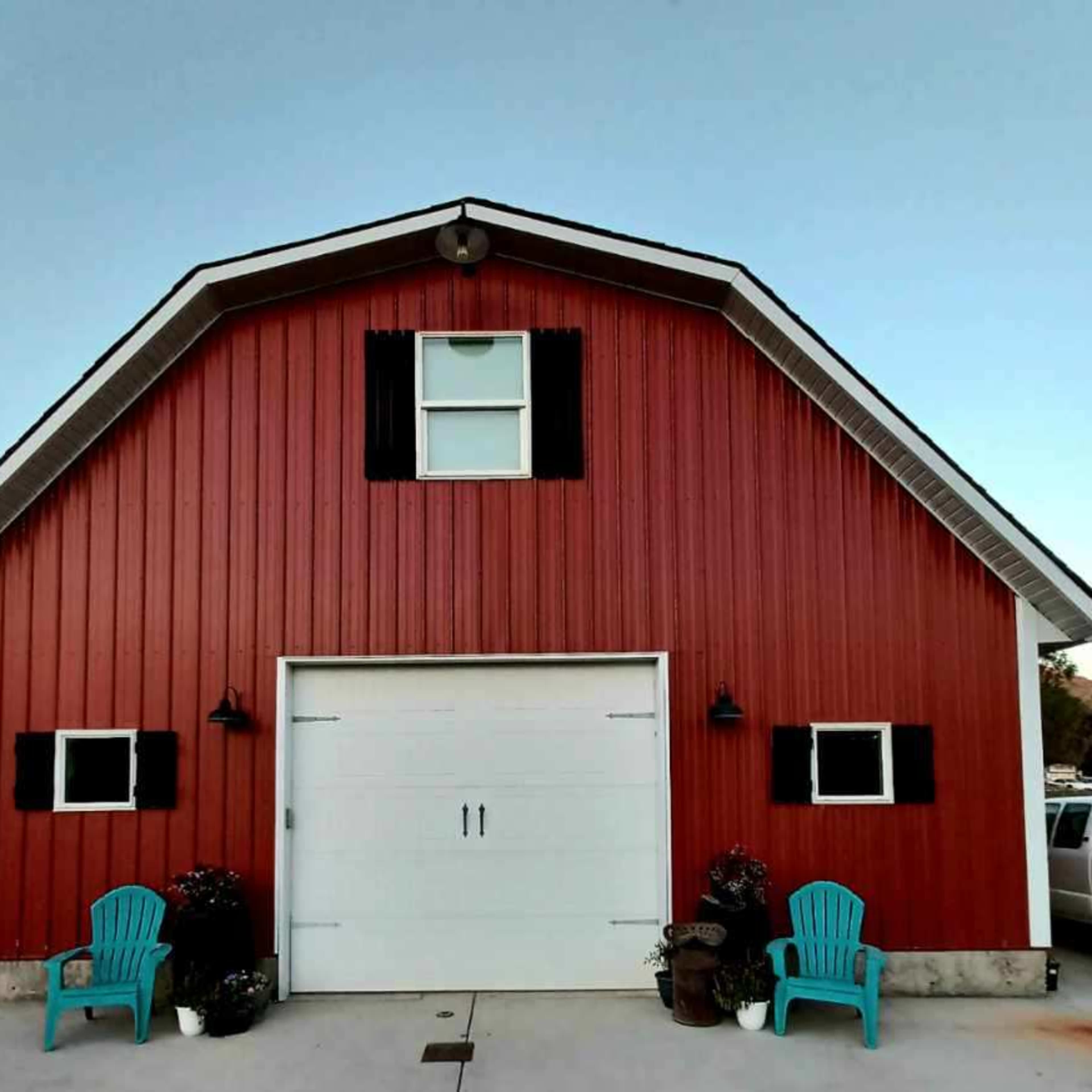 A red barn with a white garage door, flanked by black shutters and two blue chairs on either side.