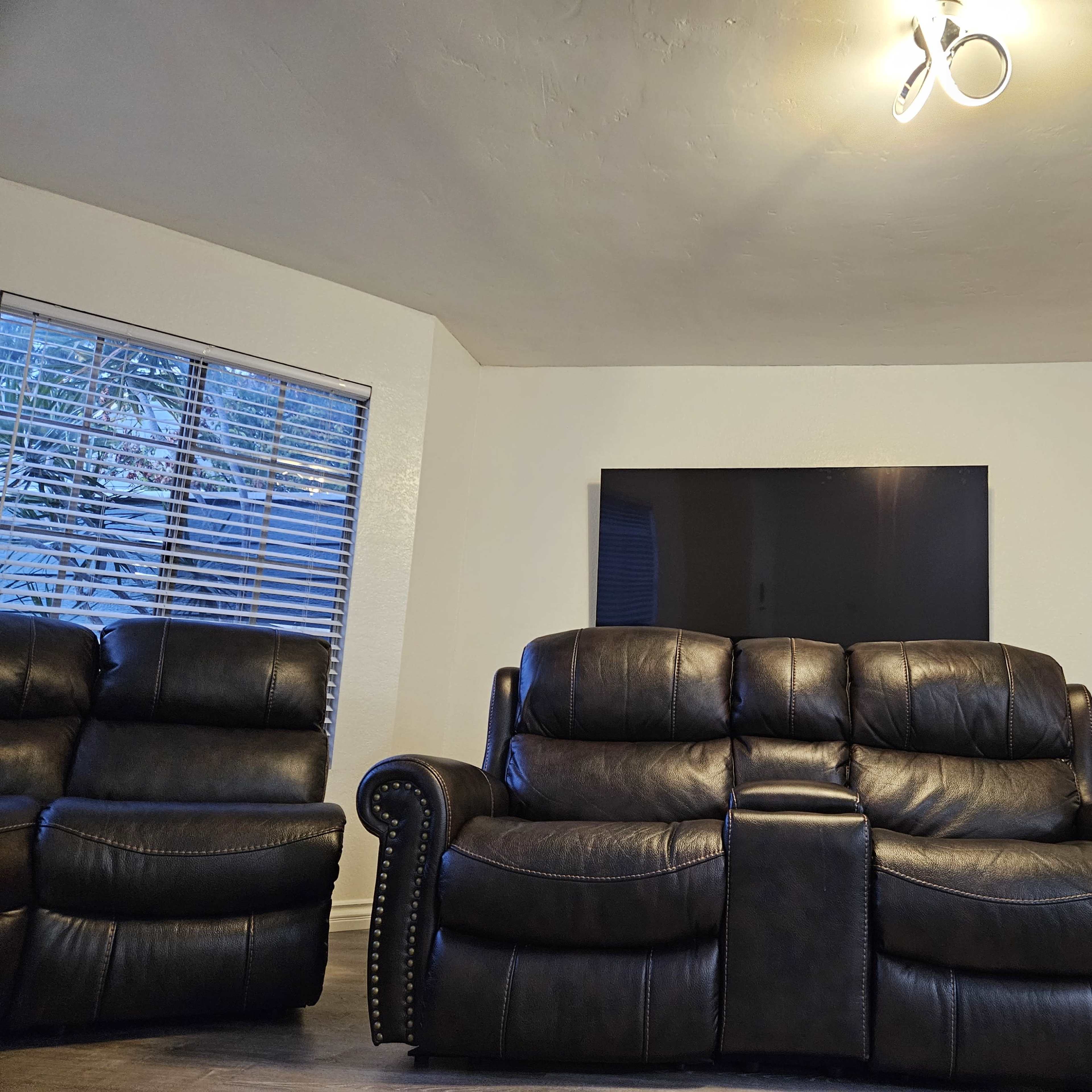 A spacious living room features a dark leather couch facing a wall-mounted television above a stone fireplace.