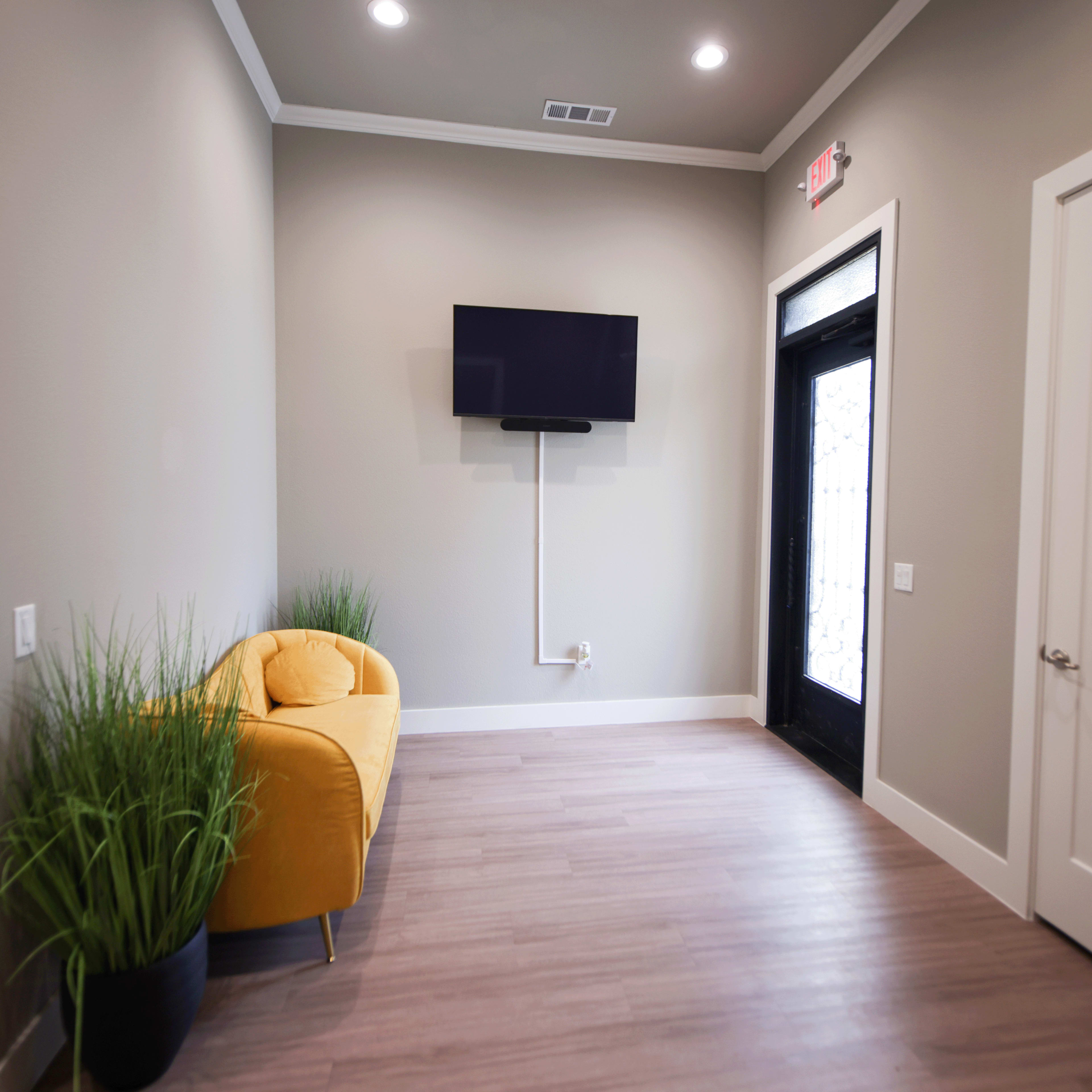 A small, modern room featuring a yellow sofa, a wall-mounted television, and a door with a large window.
