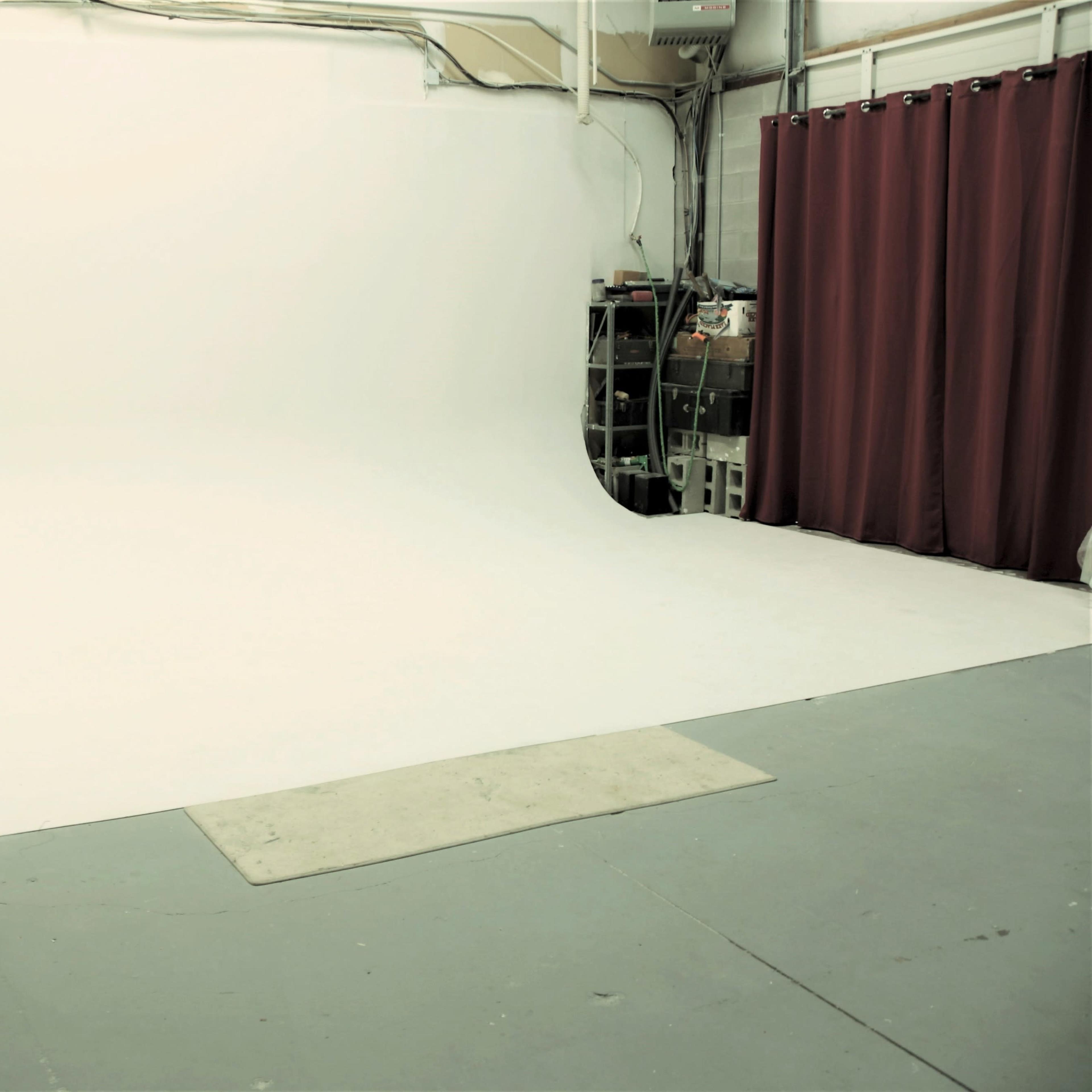 A photography studio with a seamless white backdrop, a wooden bench, and red curtains.