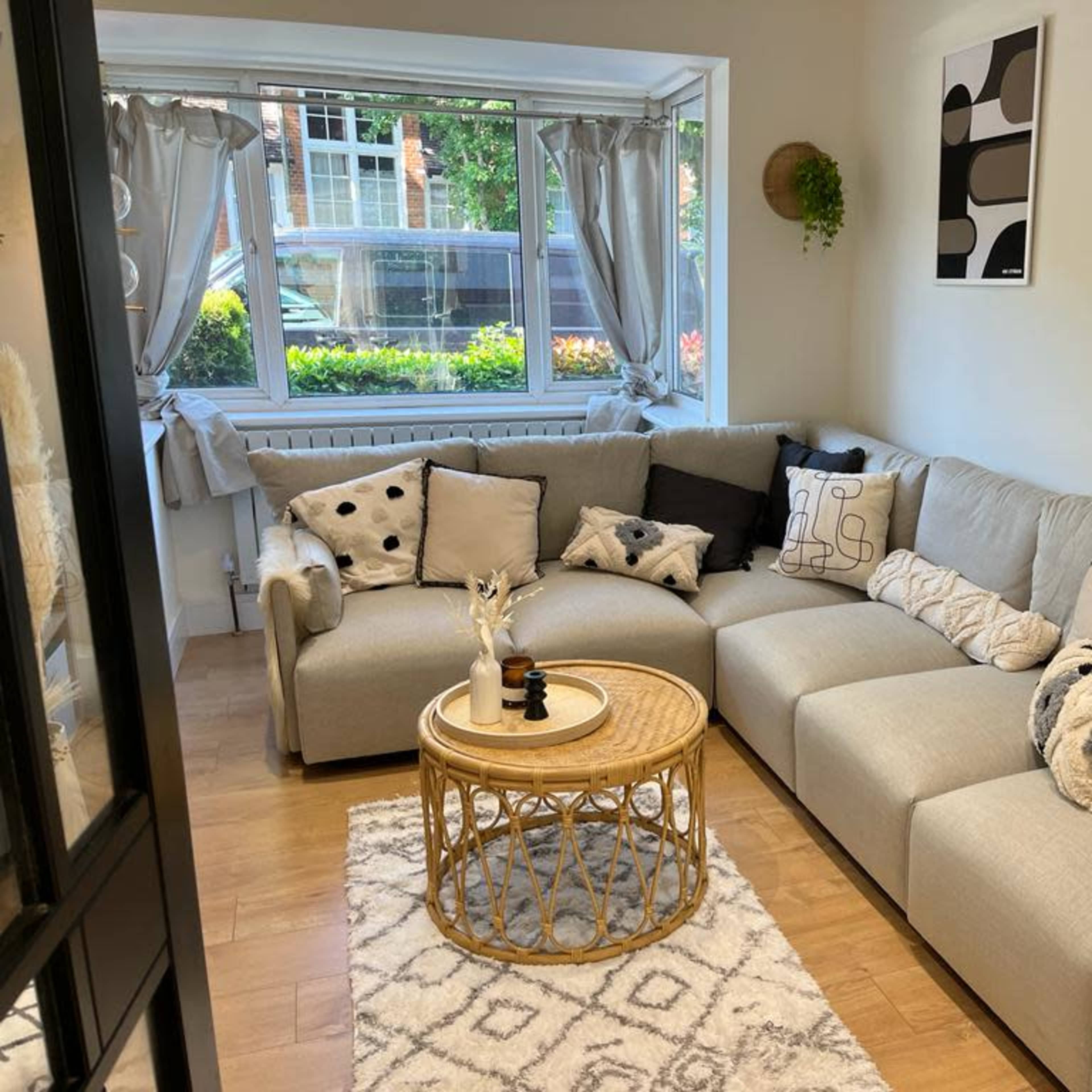 A cozy living room featuring a sectional sofa with various patterned pillows, a round coffee table, and large windows providing natural light.
