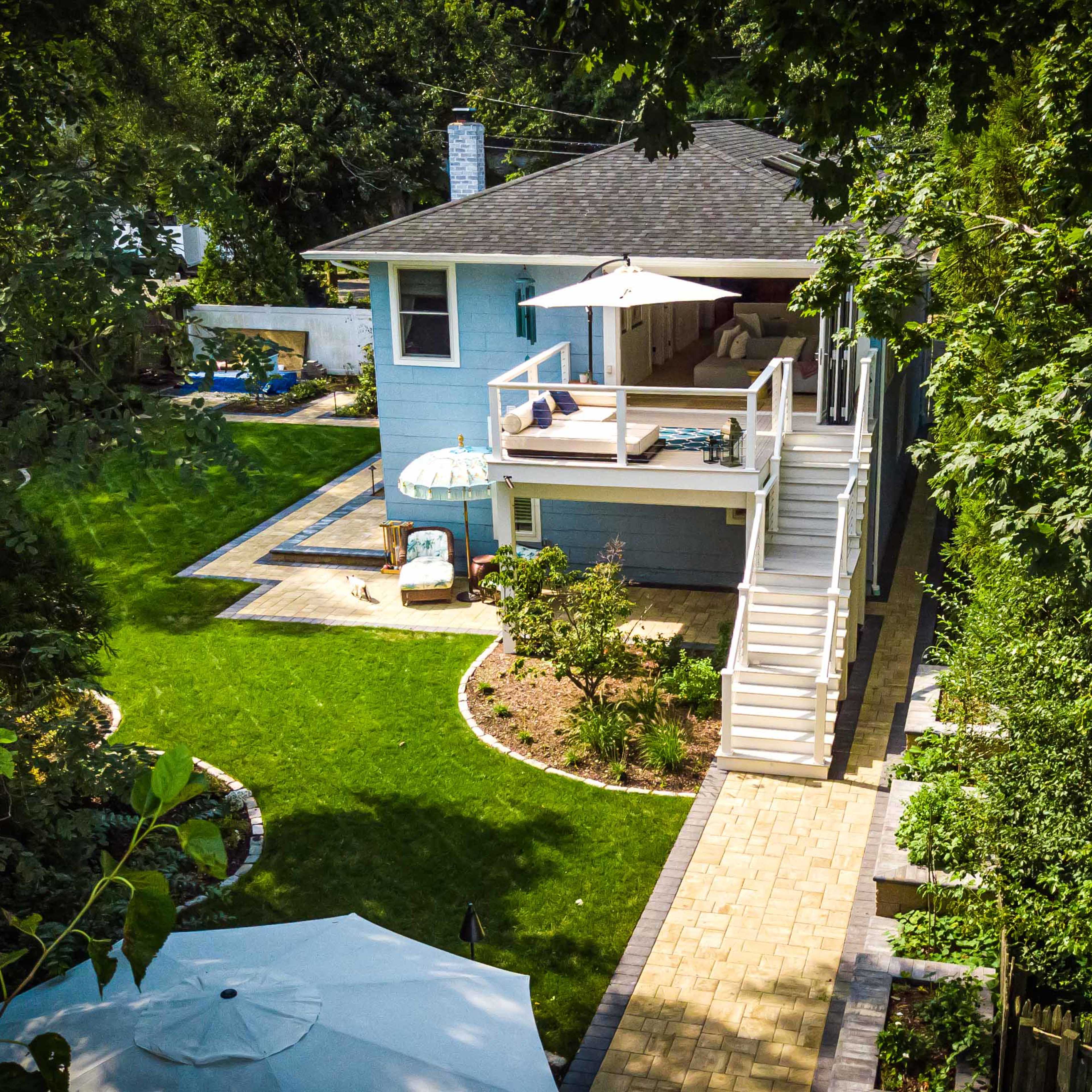 A two-story blue house with a spacious backyard, featuring a patio, a pathway, and landscaped greenery.