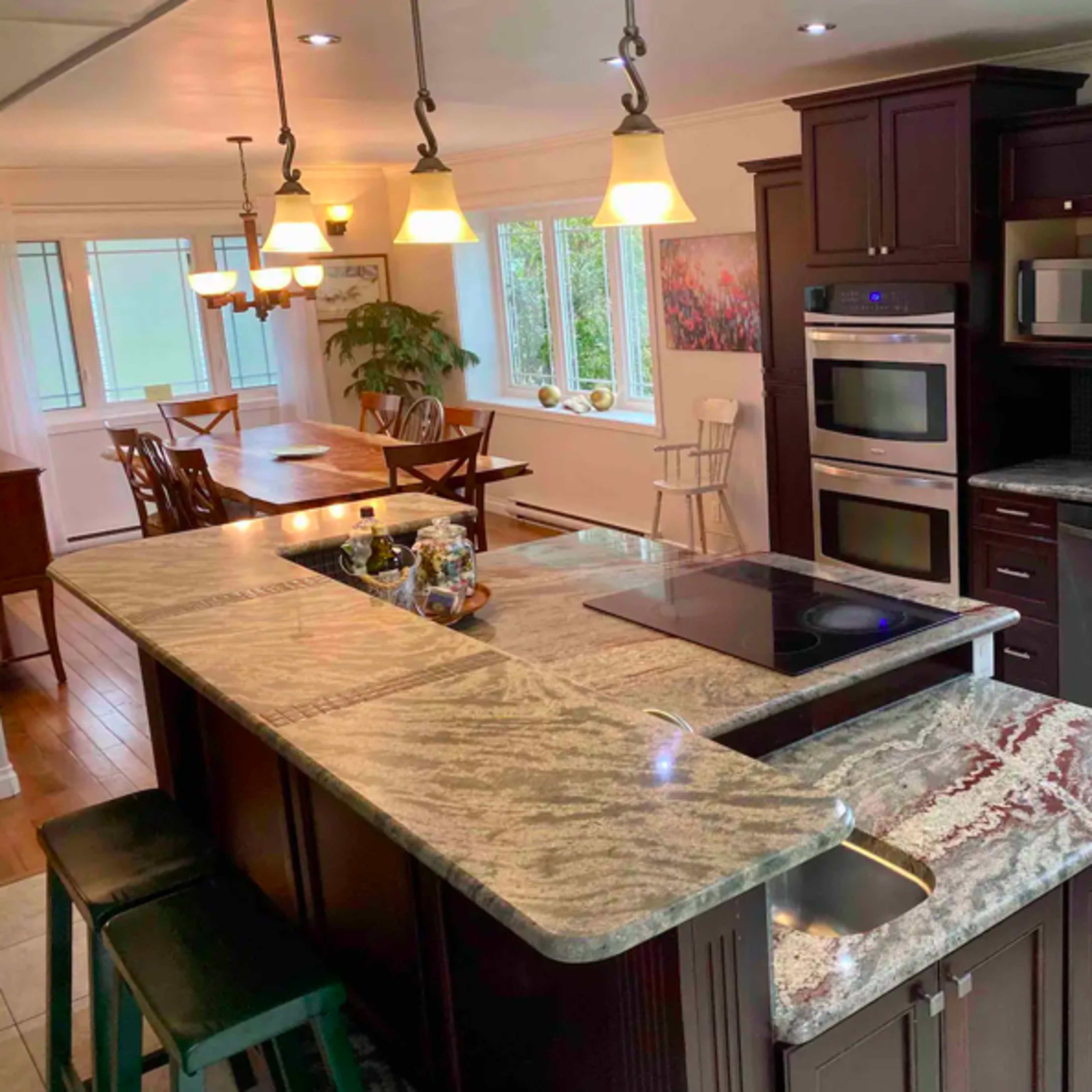 A modern kitchen with dark wood cabinetry, a large granite countertop island, and multiple windows allowing natural light to enter.