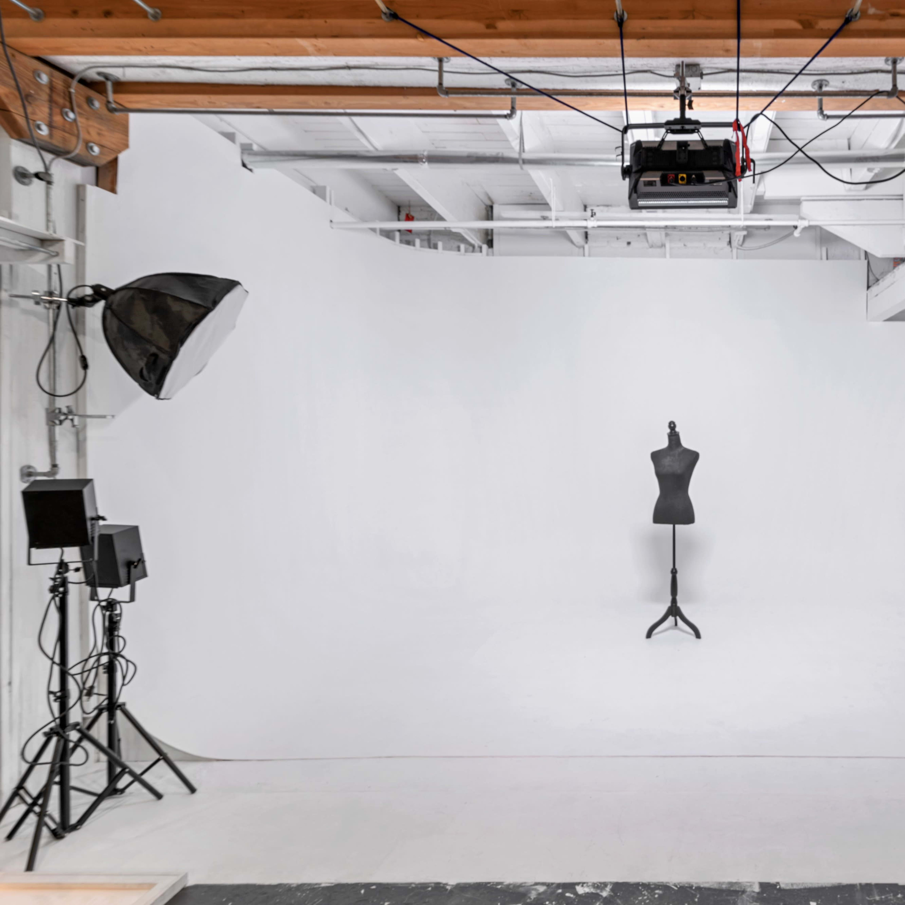 A photography studio features a white backdrop, a dress form on a stand in the center, and various lighting equipment arranged around the space.