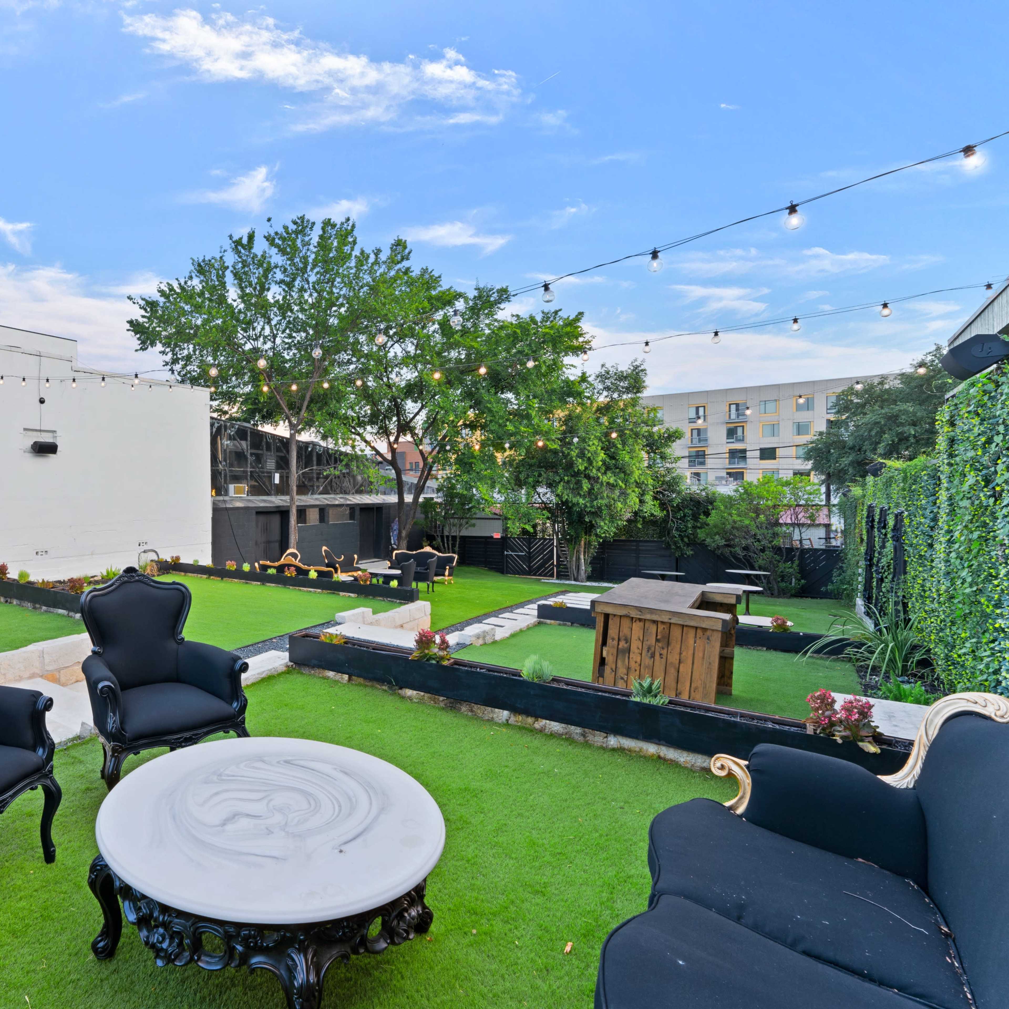 A landscaped outdoor space featuring black seating, a circular table, and string lights above a grassy area.