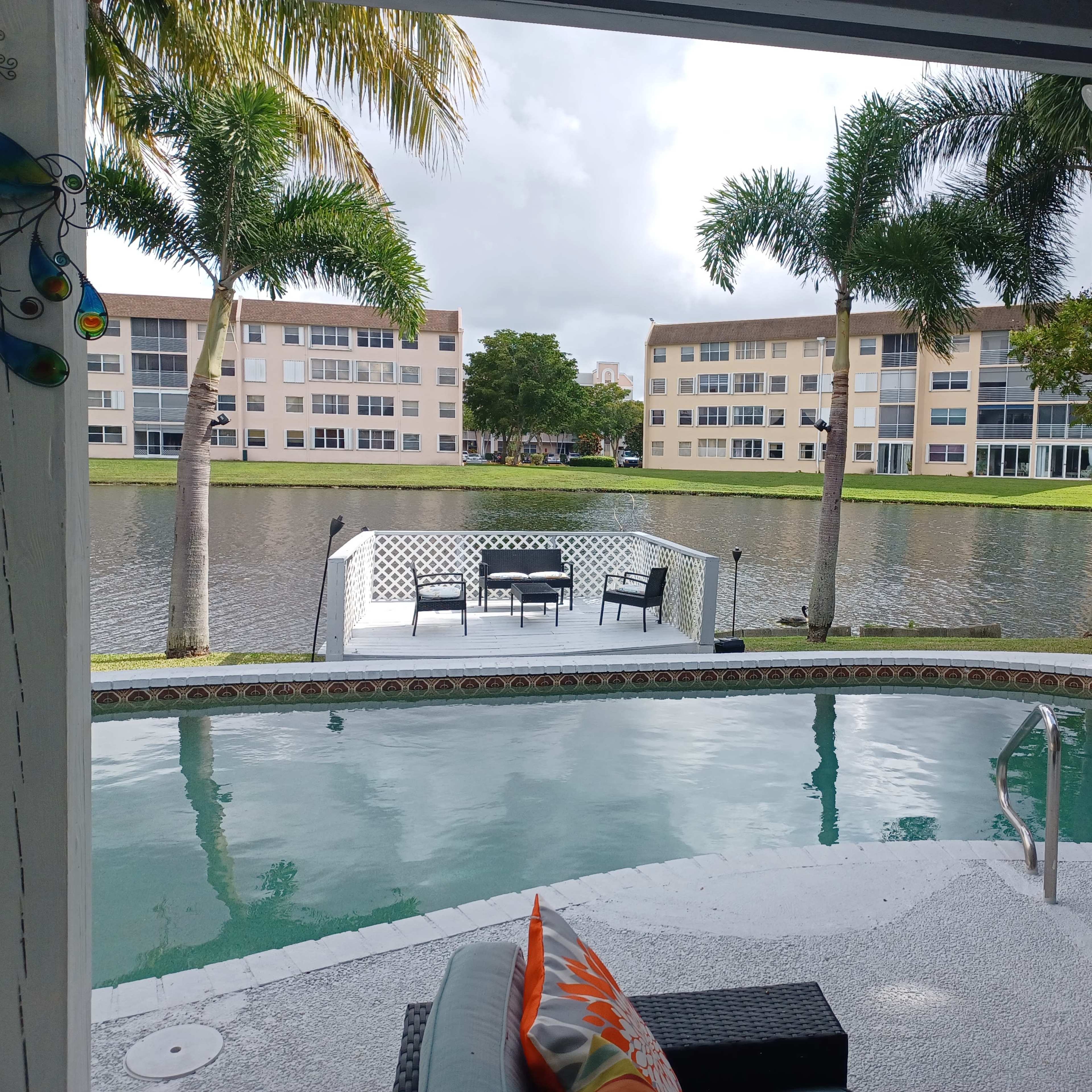 A pool area with a view of a calm lake and several apartment buildings in the background.