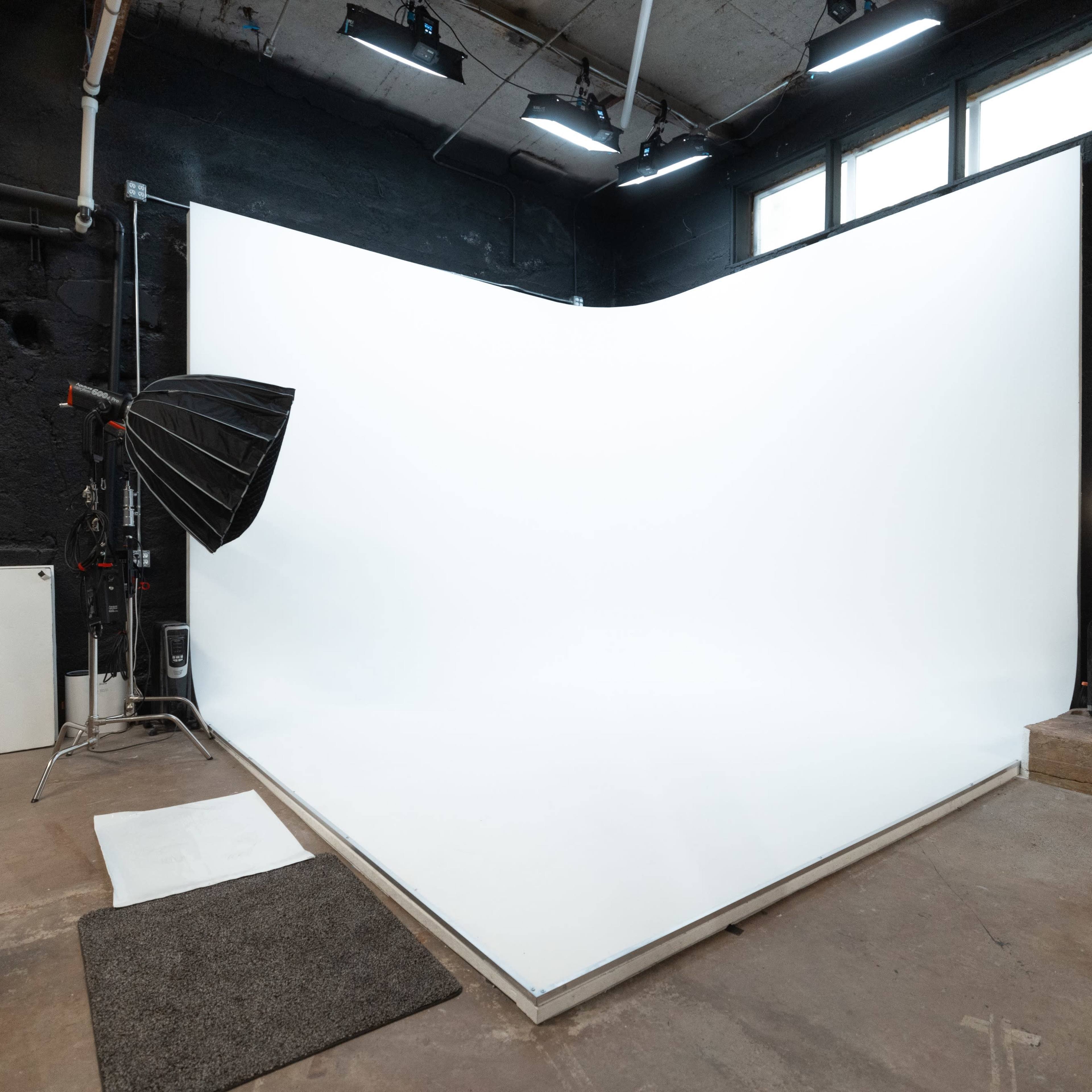A photography studio with a curved white backdrop, a softbox light, and concrete flooring.