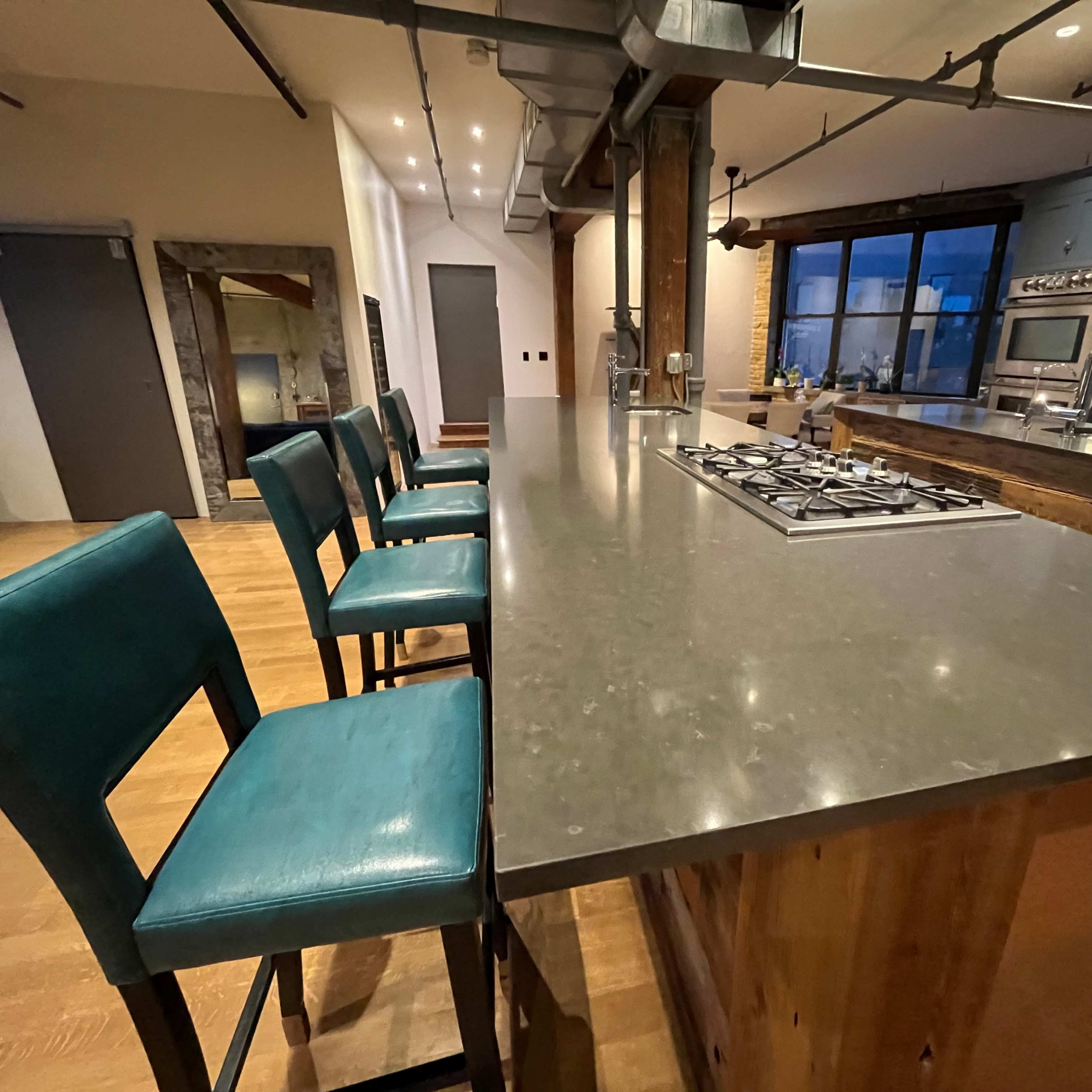 A spacious kitchen features a large island with a gas cooktop and teal bar stools lined up along one side.