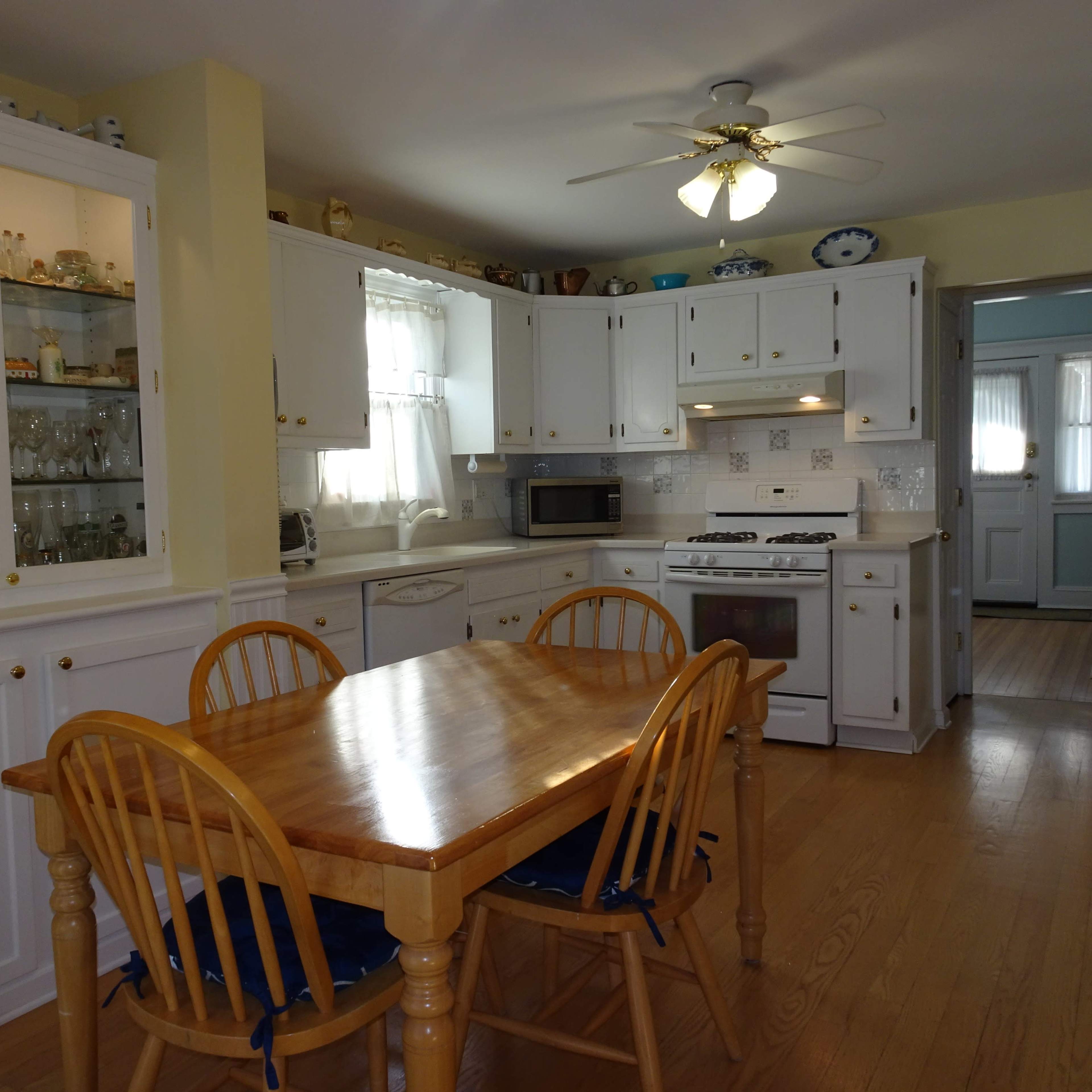 A bright kitchen with white cabinetry, a wooden dining table, and a window allowing natural light to enter.