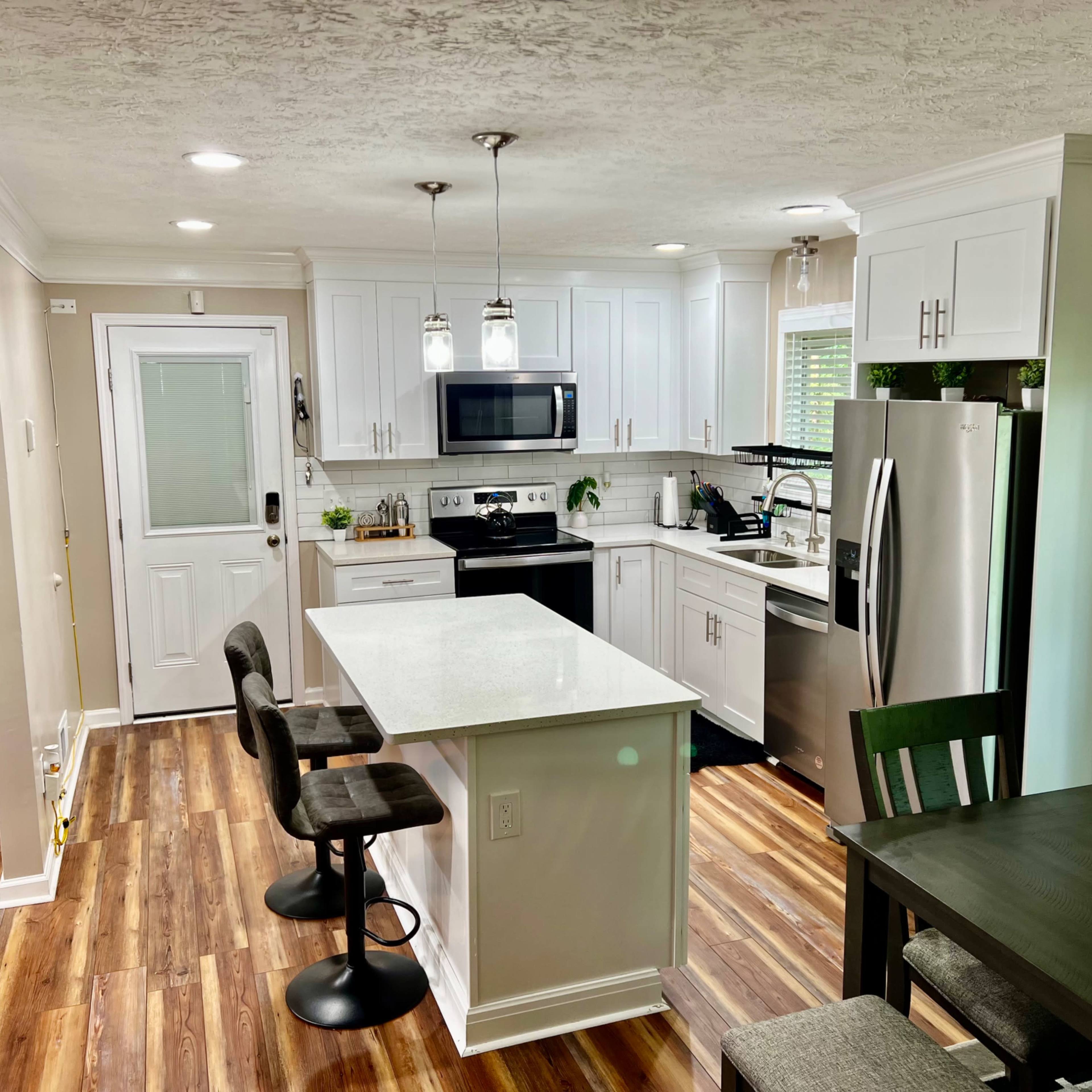 A modern kitchen with white cabinets, stainless steel appliances, a central island with bar stools, and hardwood flooring.