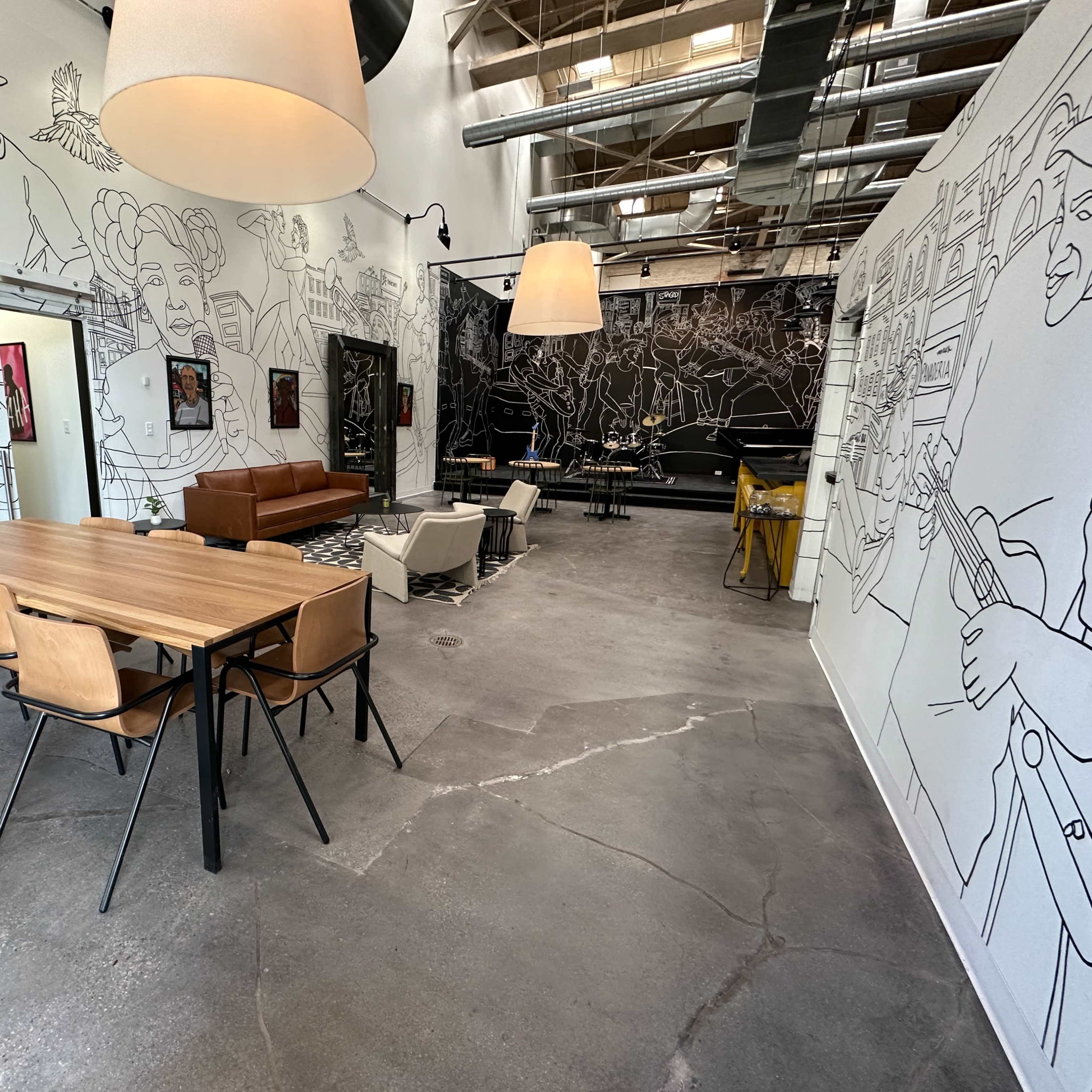 An industrial-style interior with a dining table, chairs, a brown sofa, and large murals on the walls.