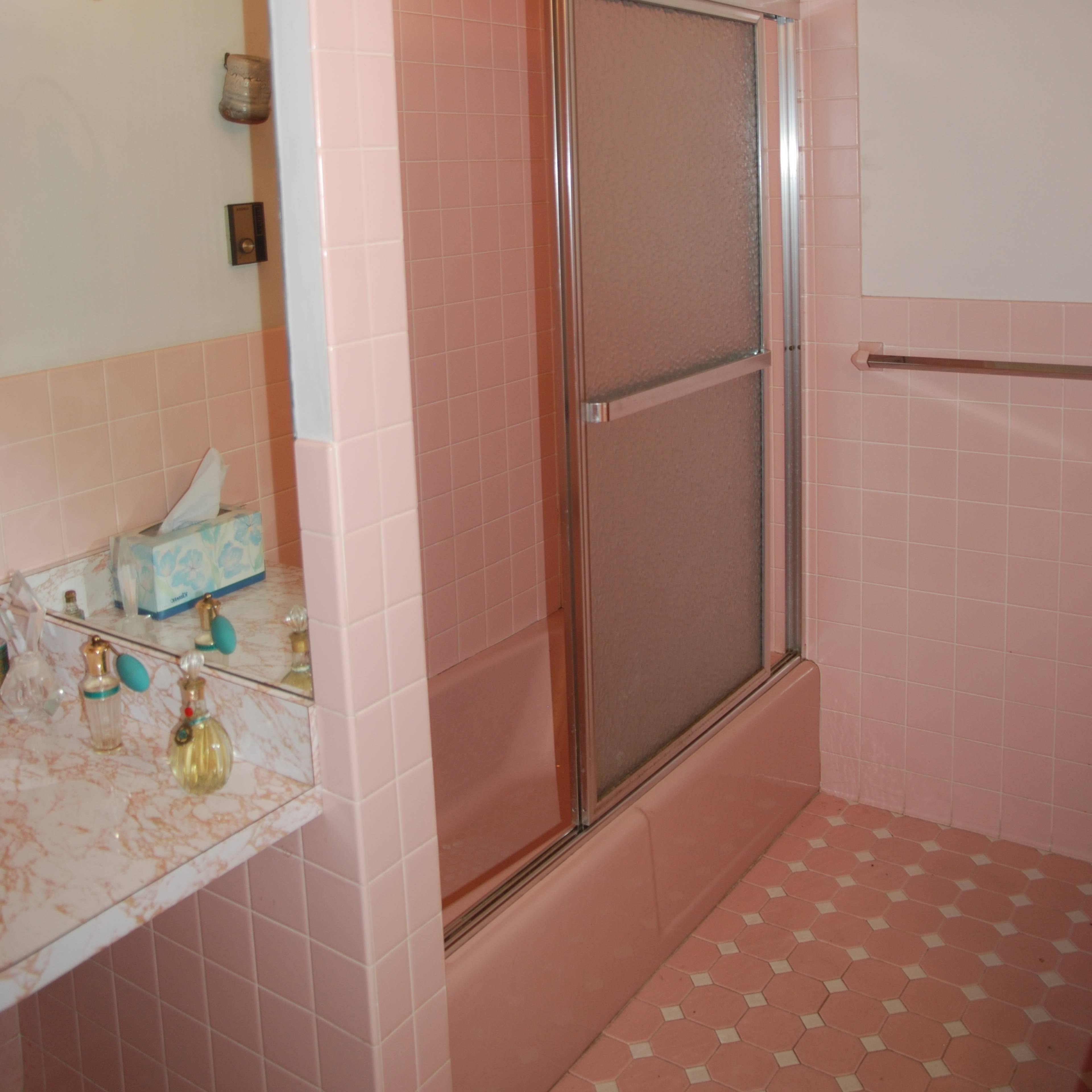 The bathroom features pink tiles, a glass shower enclosure, and a marble vanity with toiletries.