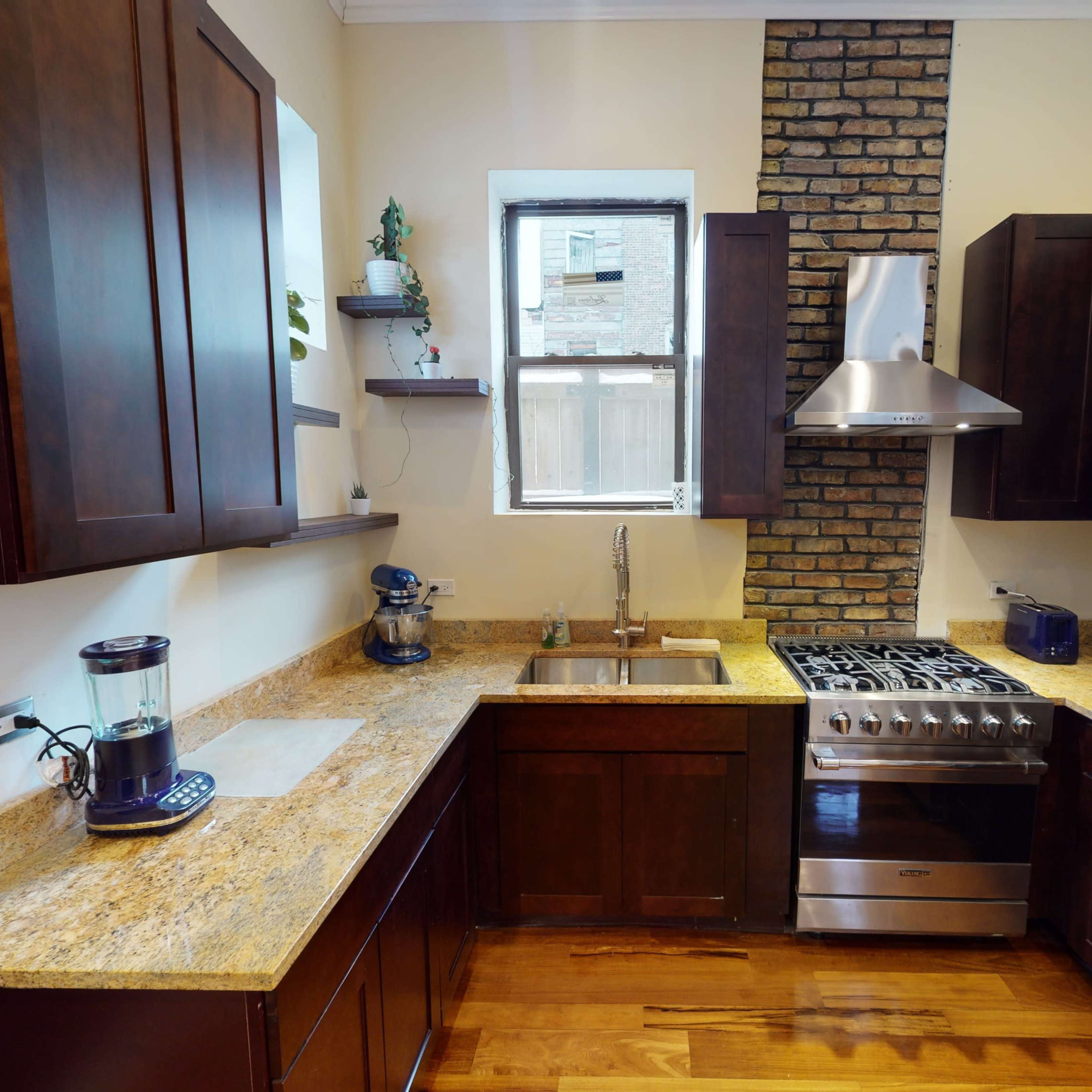 A modern kitchen featuring dark wooden cabinets, a granite countertop, a stainless steel stove, and a window with a view.