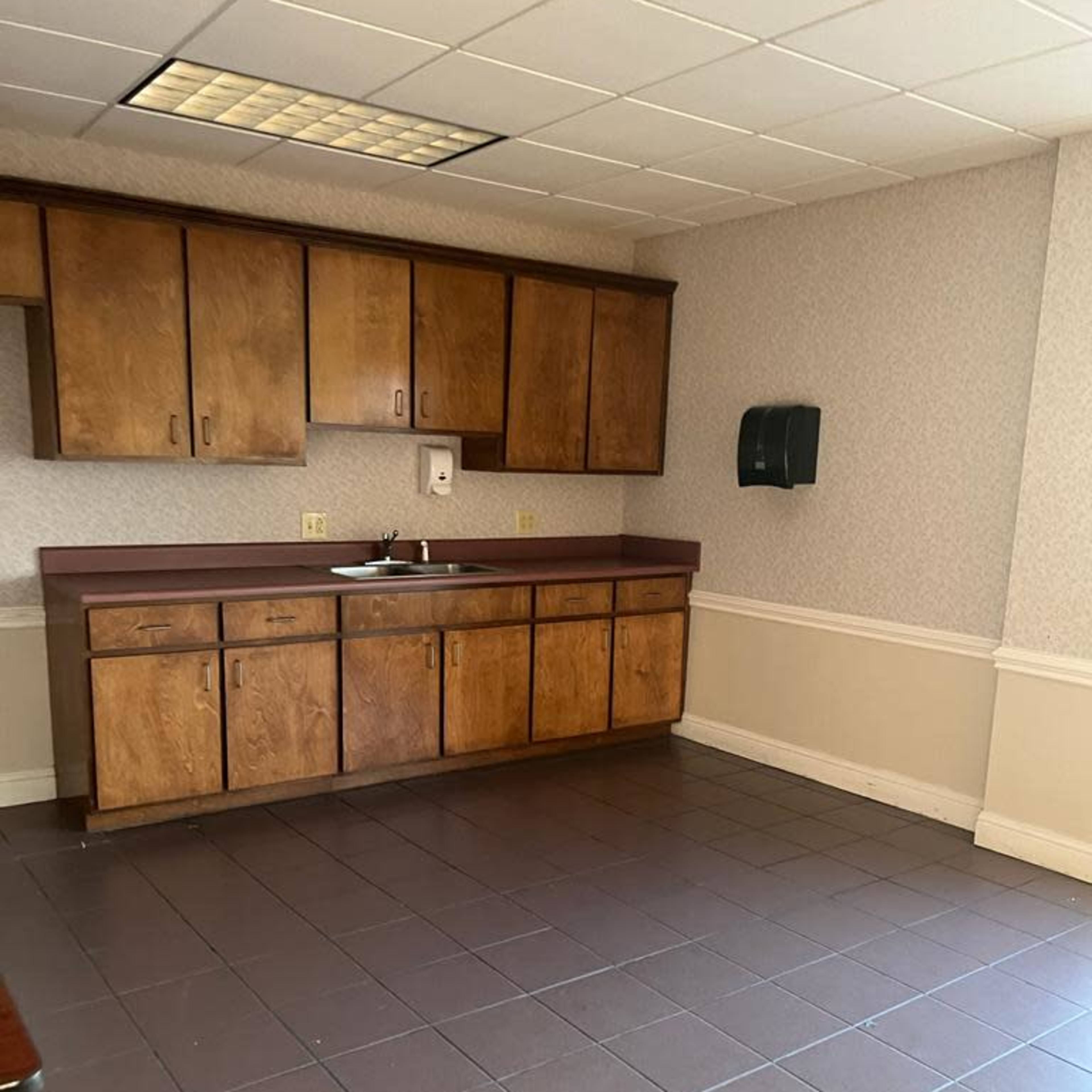 A small kitchen area featuring wooden cabinets, a sink, and a tiled floor.