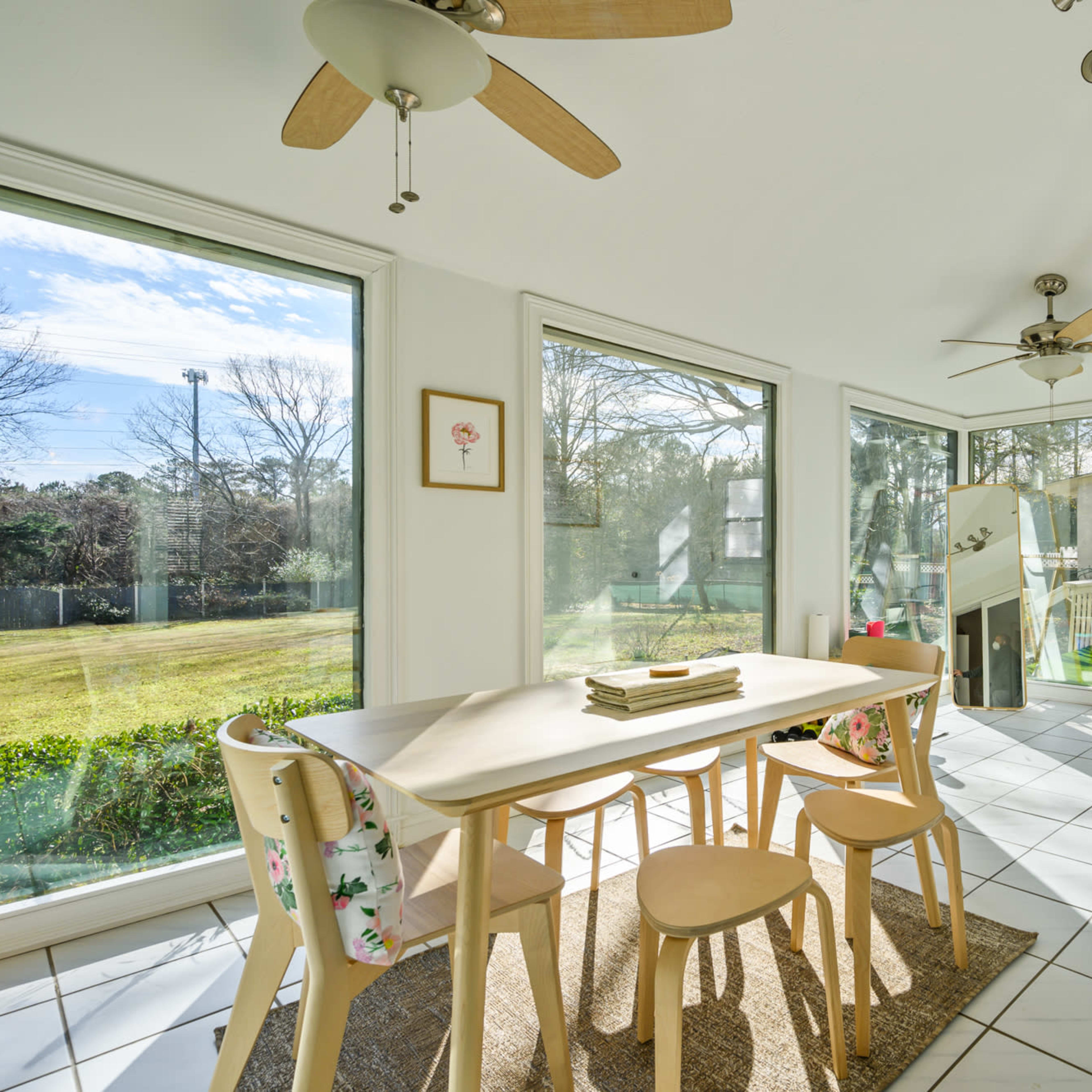A bright sunroom features large windows, a table with four chairs, and a door leading to an outdoor area.