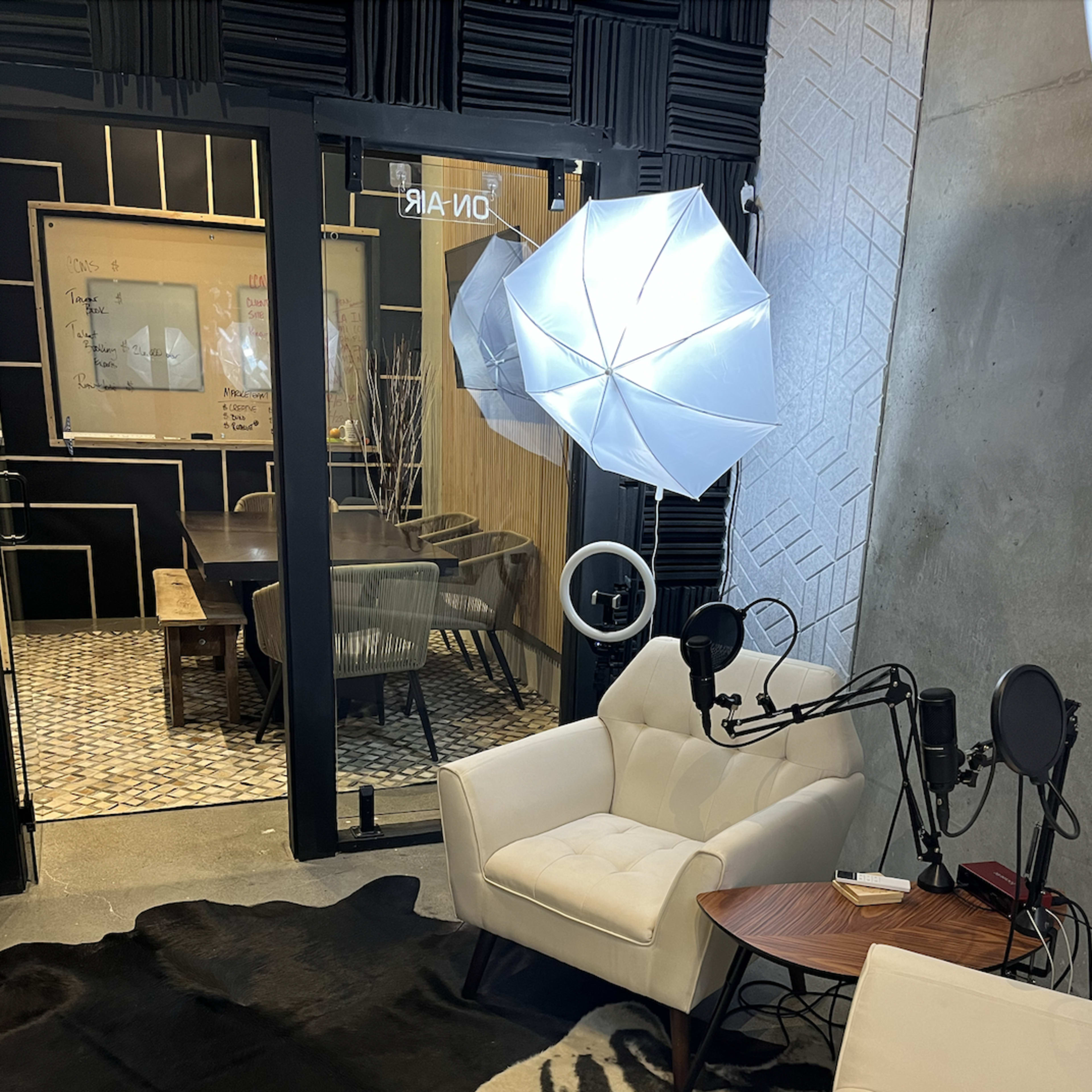 A modern recording studio setting with two white chairs, a wooden table, studio lights, and soundproof walls.