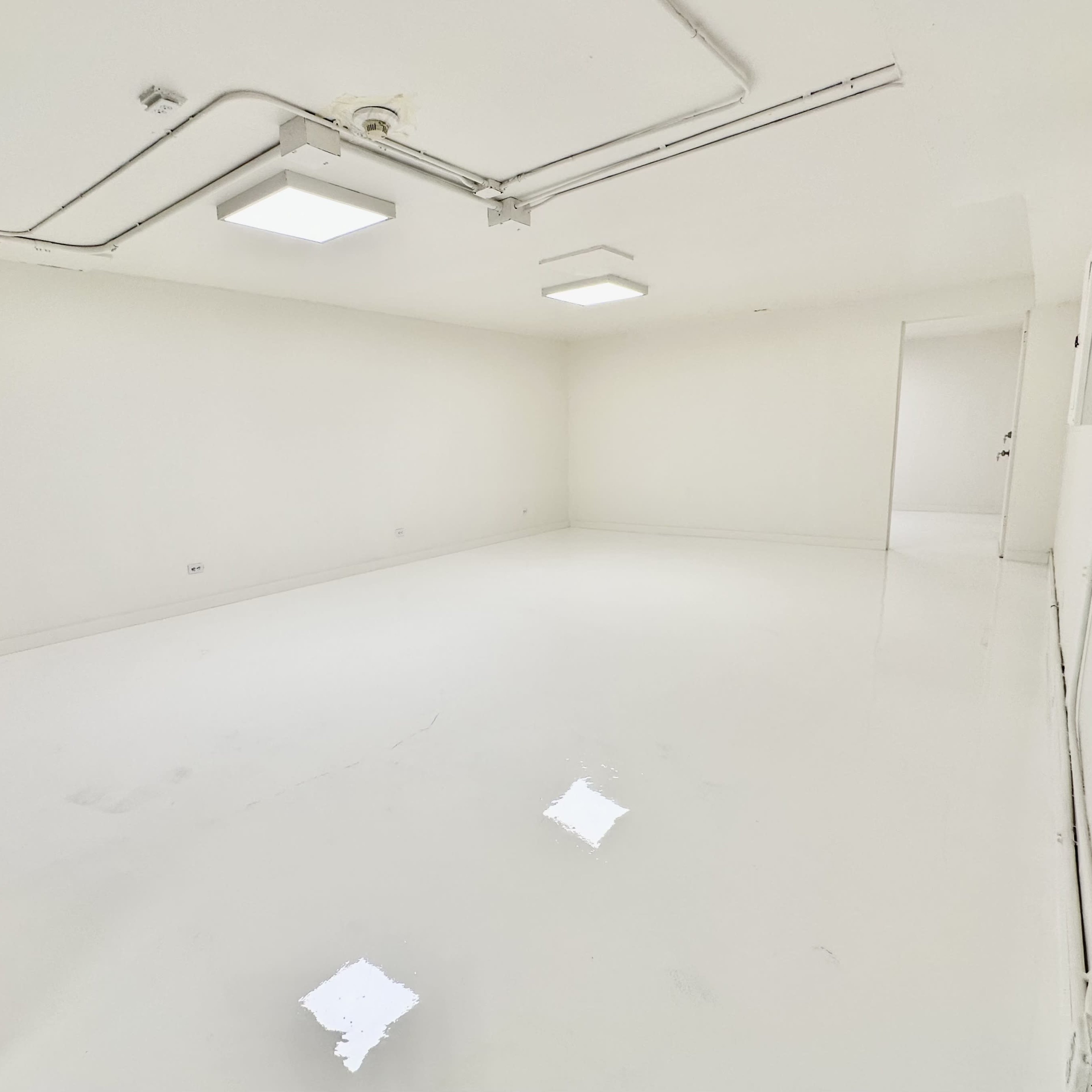An empty, well-lit room with white walls and a glossy white floor.
