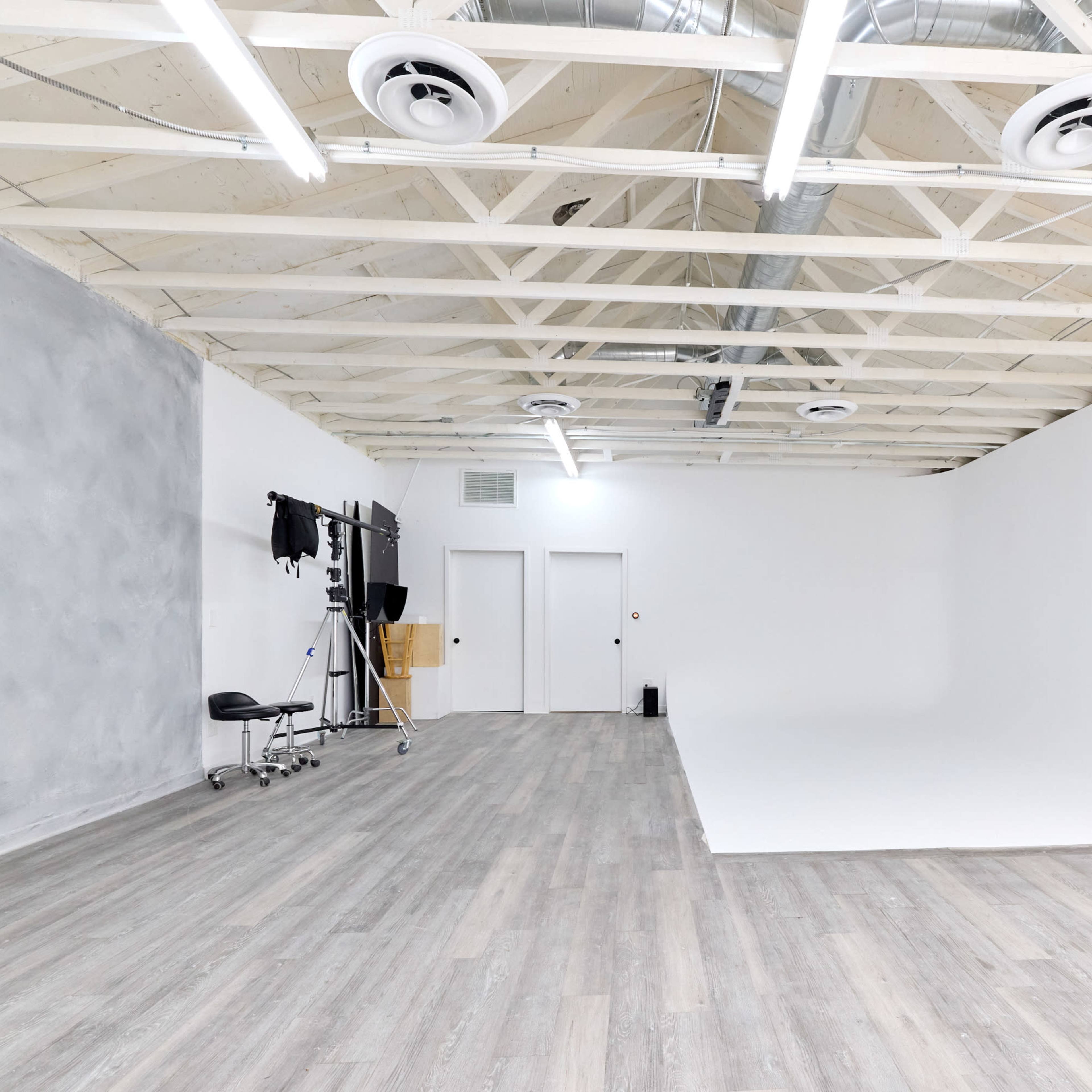 A spacious photography studio featuring a white backdrop, wooden flooring, and a few pieces of equipment against one wall.