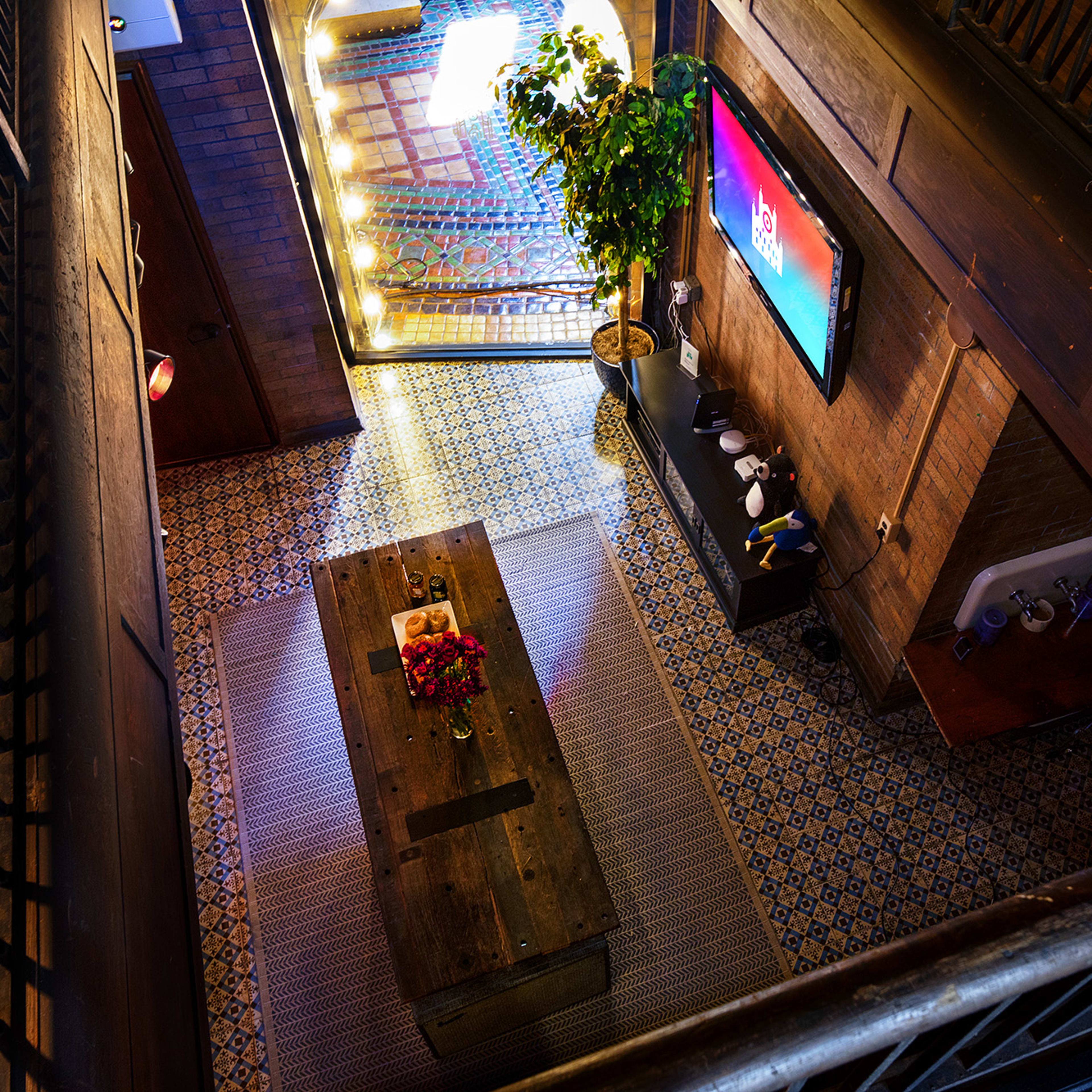 An indoor space with a wooden coffee table, a plant, a large television mounted on the wall, and patterned tiles on the floor.