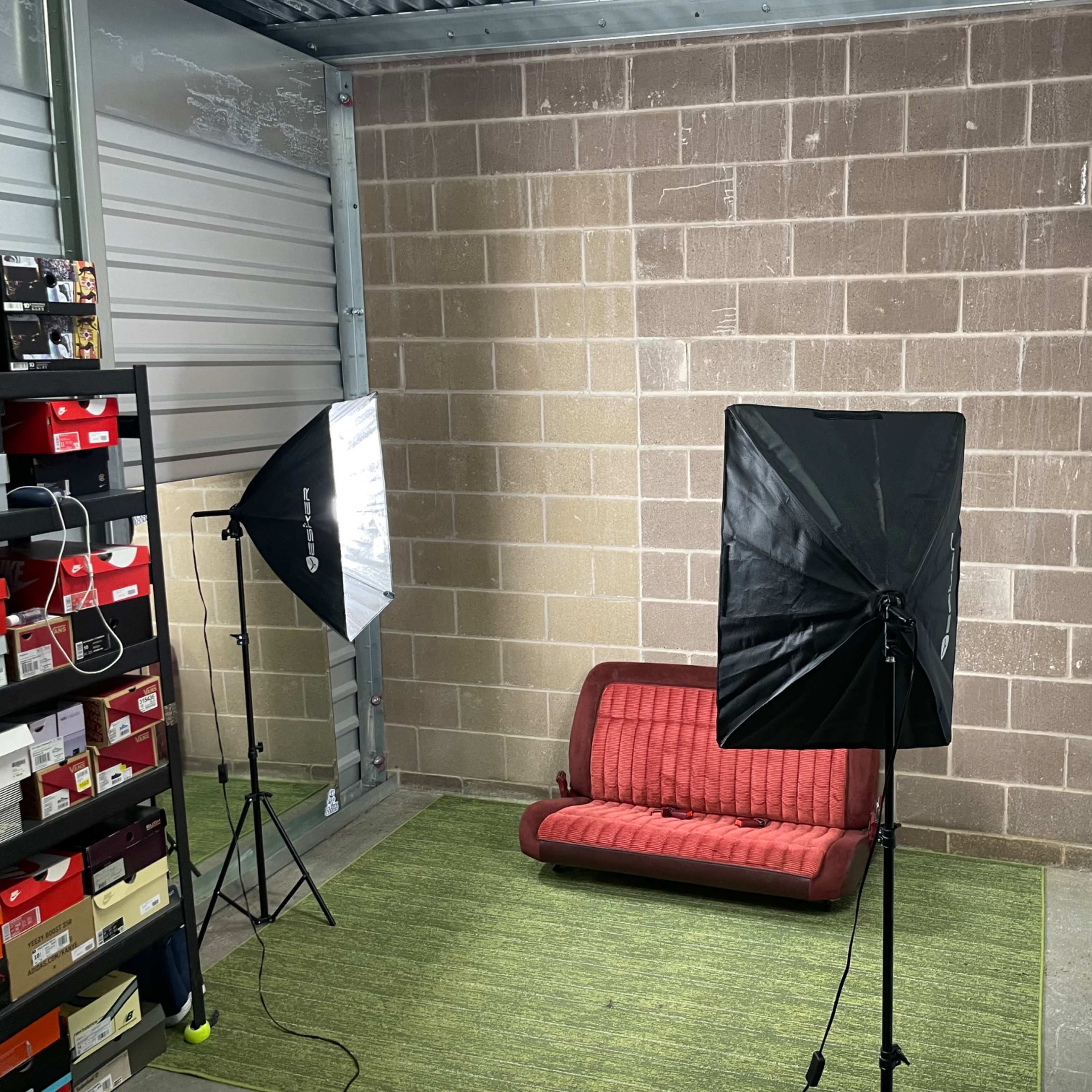 A small storage unit featuring a red couch, two softbox lights, and shelves filled with boxes along one wall.