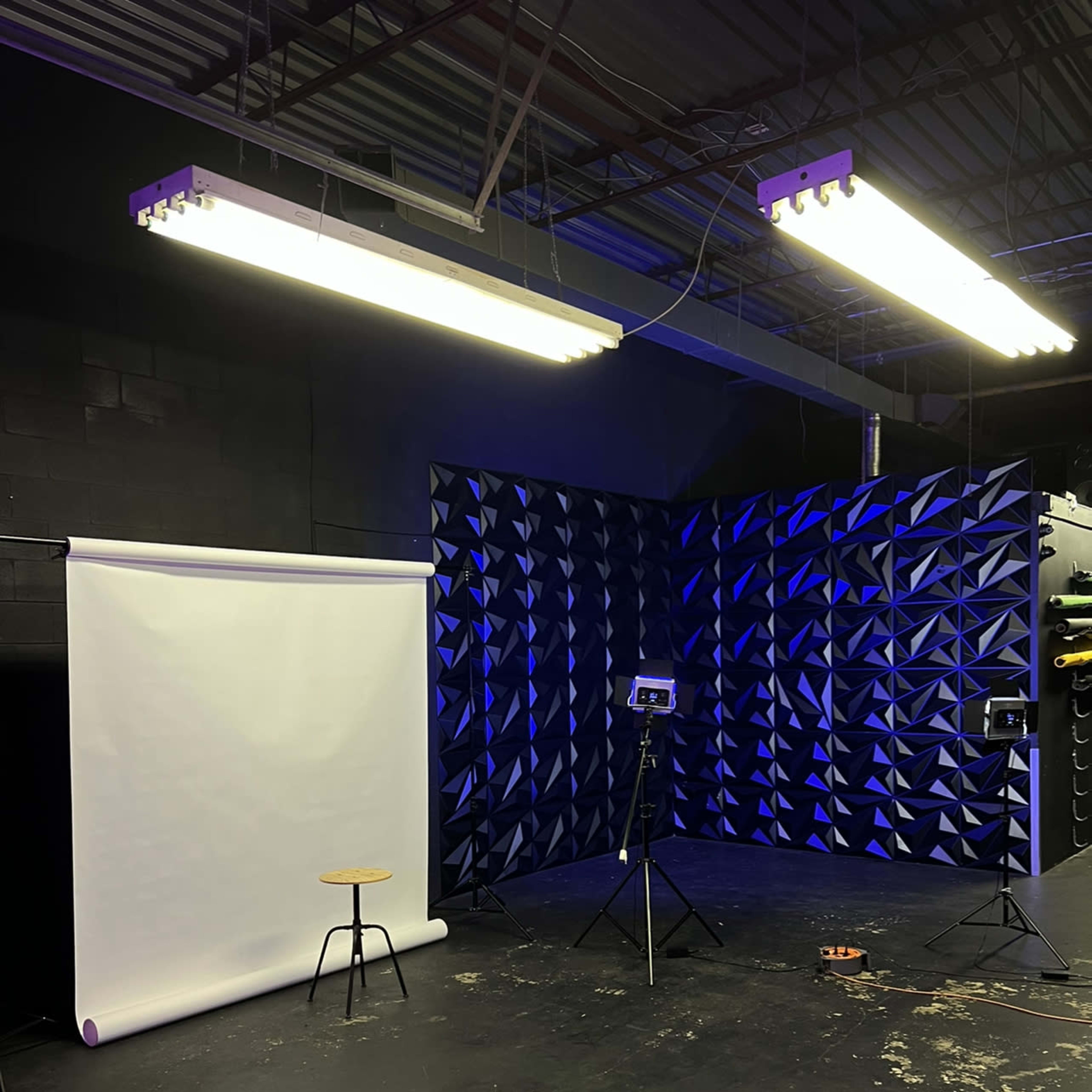 A photography studio with a white backdrop, a stool, and two lighting setups against a textured blue wall.
