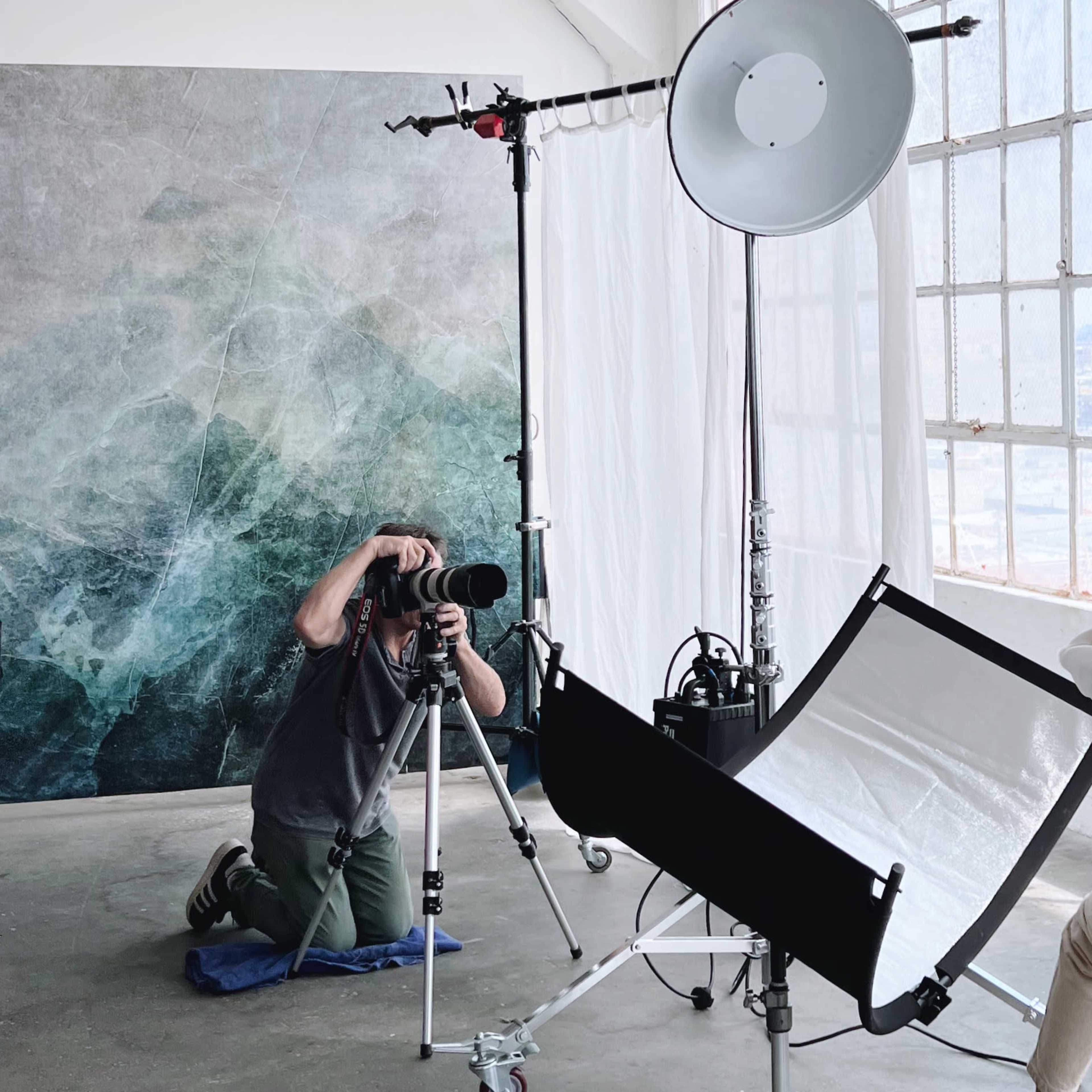 A photographer captures images of a model in a studio setting with large windows and a backdrop.
