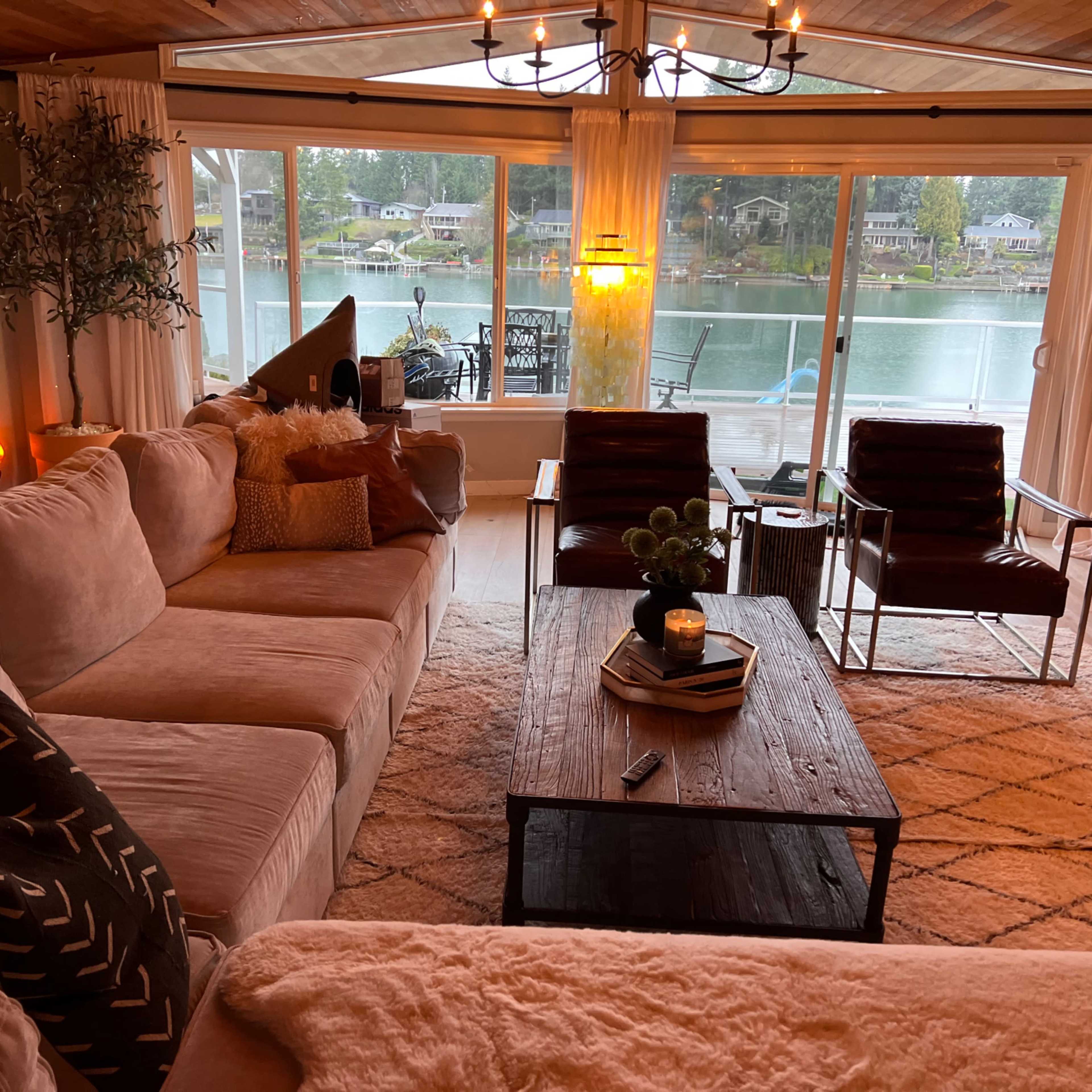 The living room features a large sectional couch, a wooden coffee table, and a view of a lake through large windows.