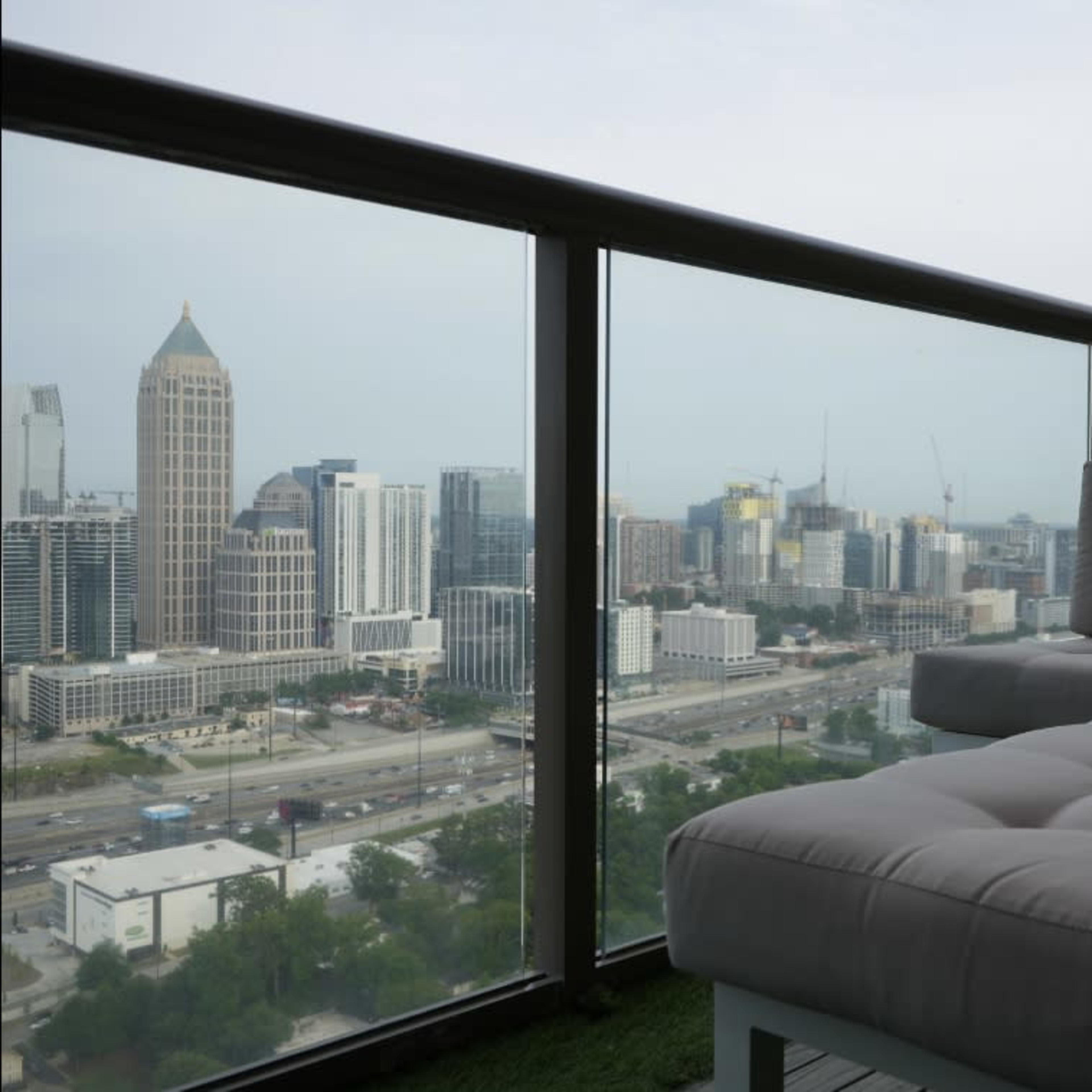 A balcony features a white cushioned seating area overlooking a city skyline with tall buildings and highways below.