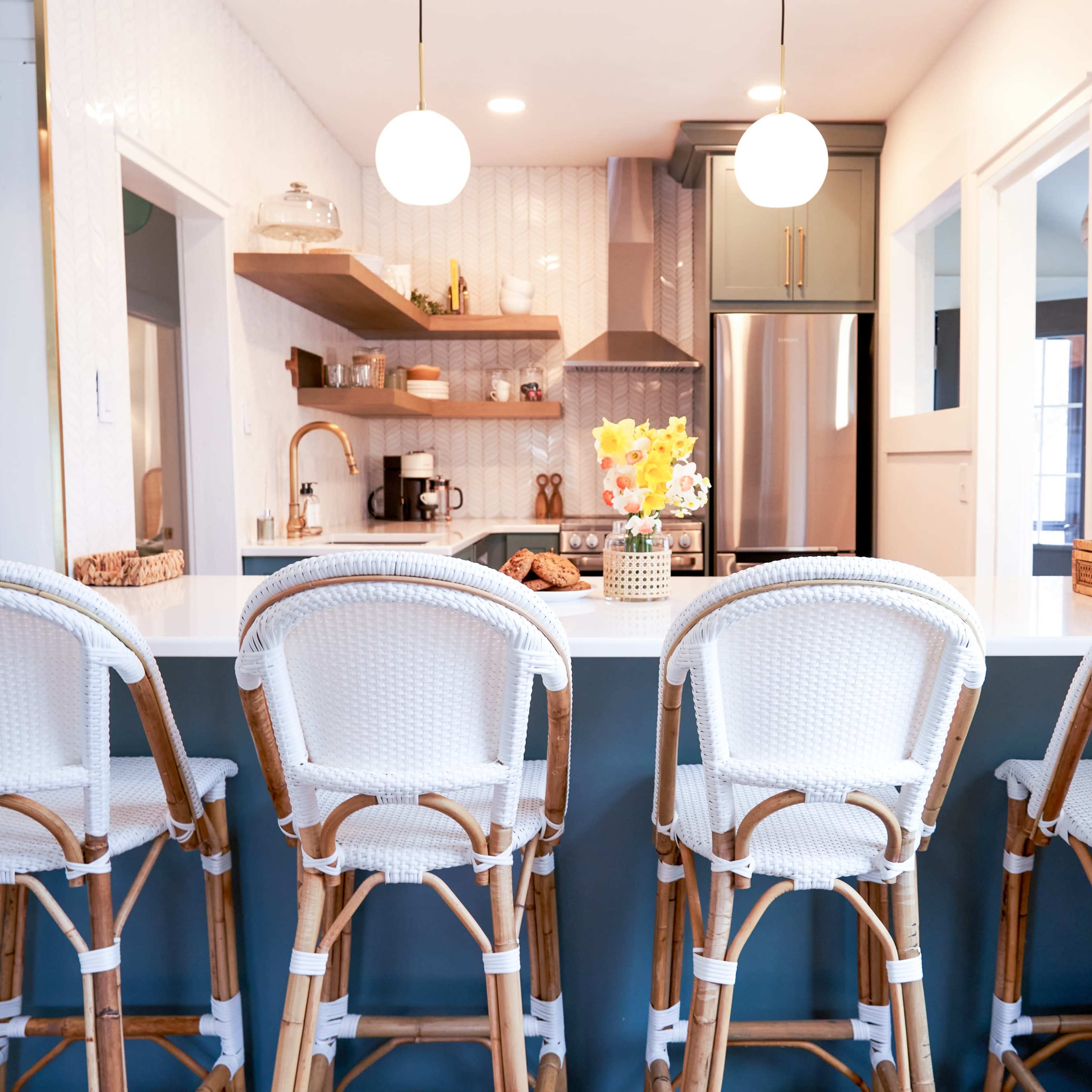A modern kitchen features a long island with four wicker bar stools, complemented by a well-organized countertop and stylish decor.