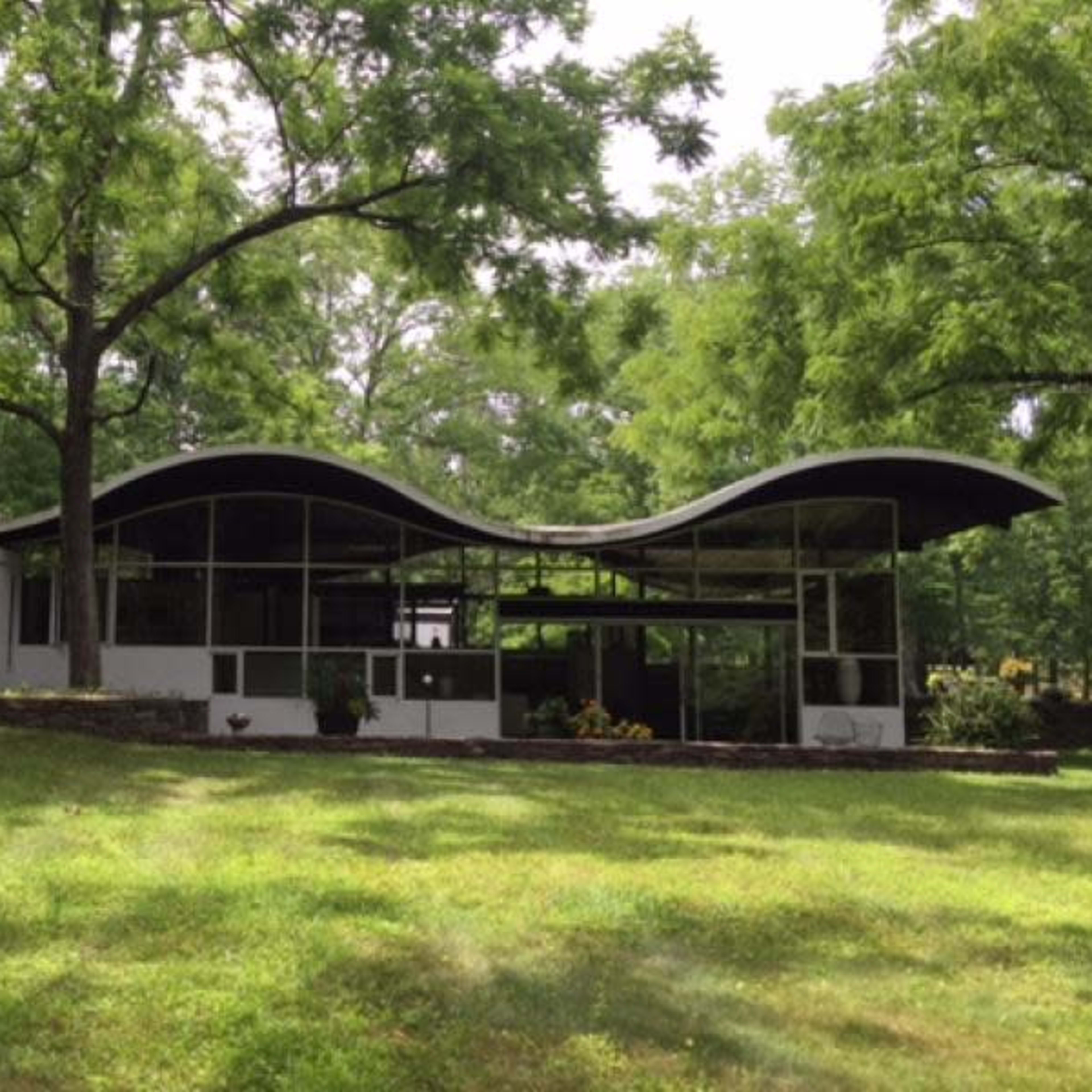 A modern building with a wavy roof, surrounded by greenery and trees in a park-like setting.