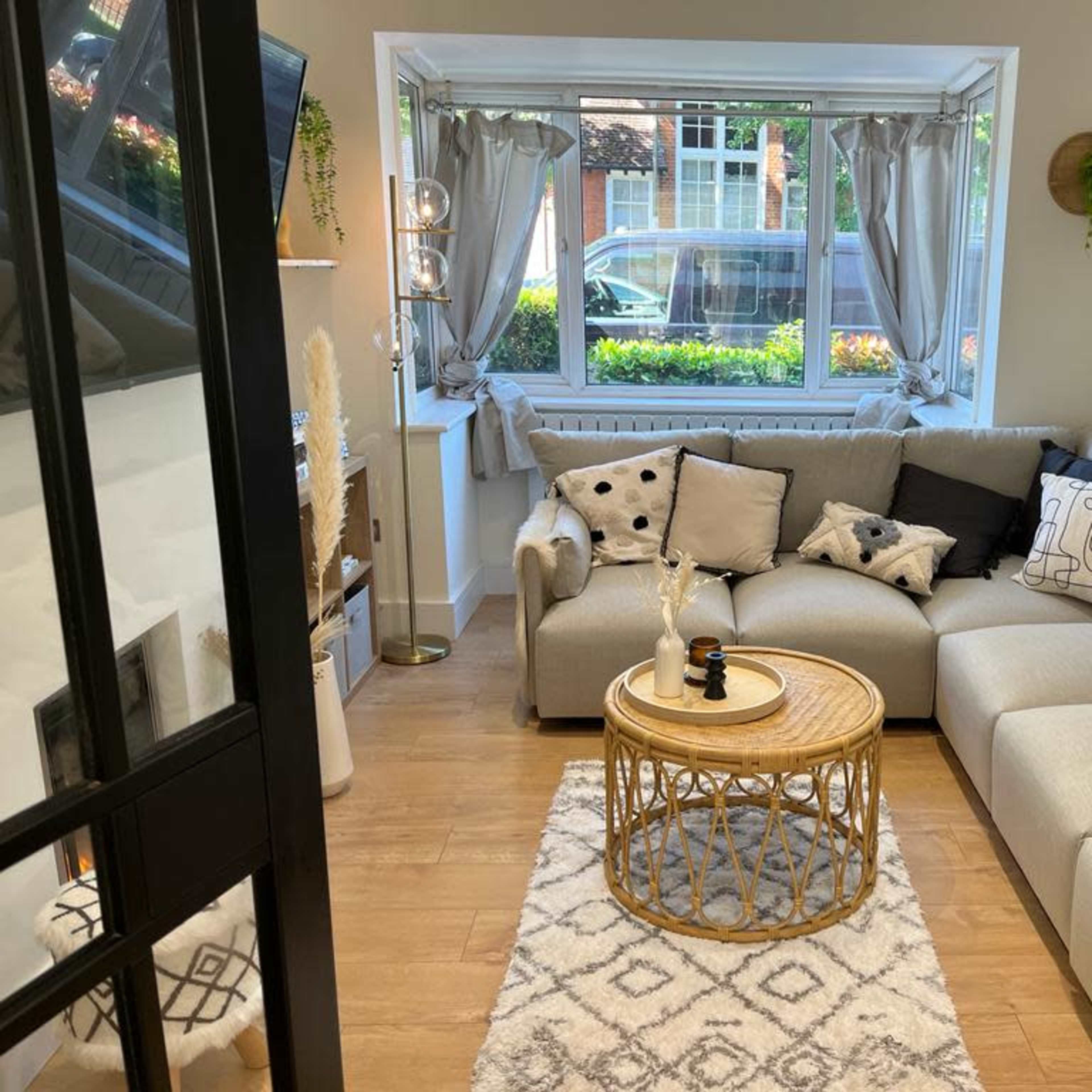 A modern living room with a sectional sofa, a round coffee table, decorative throw pillows, and large windows overlooking a green park-like area.