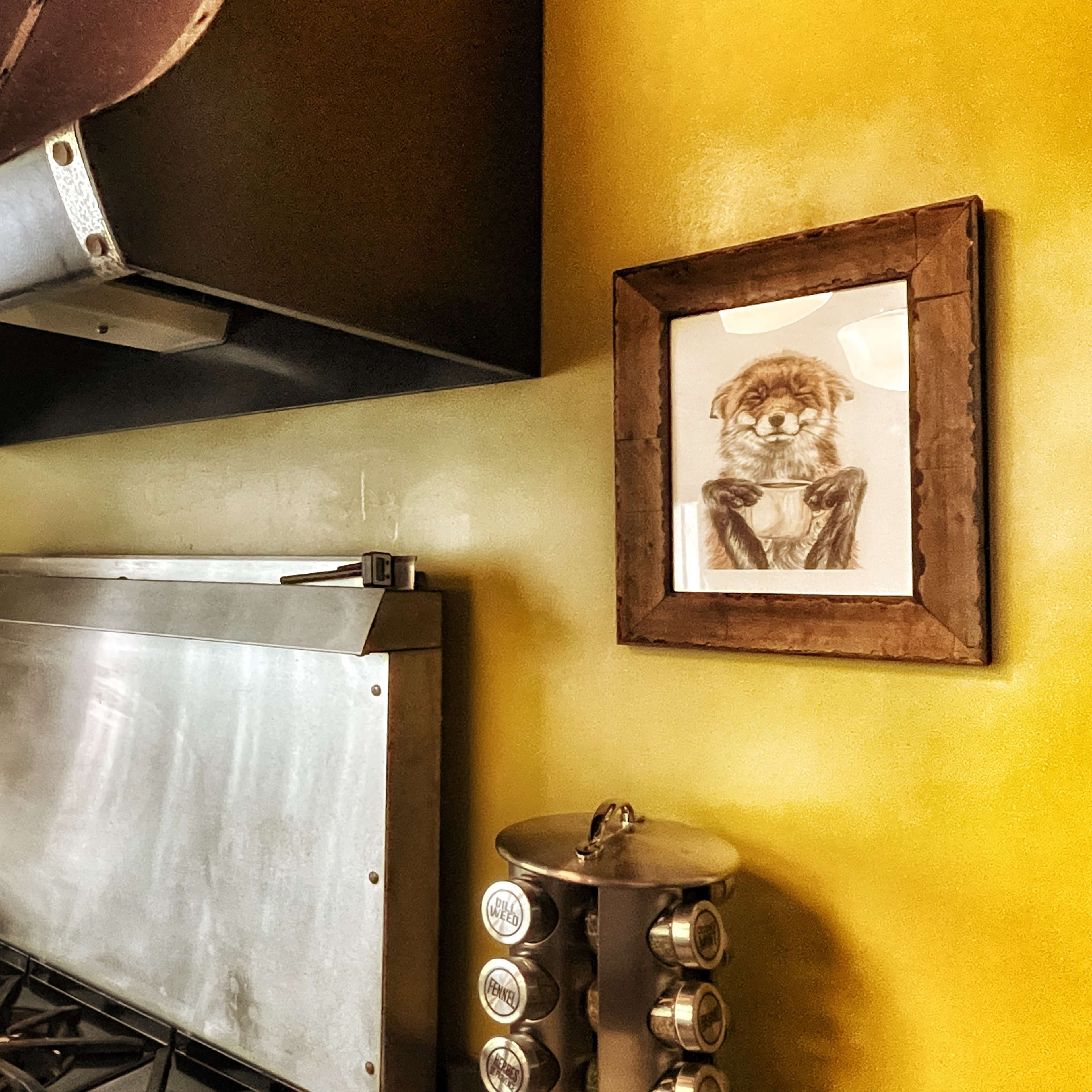 A kitchen with a stainless steel stove, a black range hood, and a framed picture of a lion holding a cup on a yellow wall.