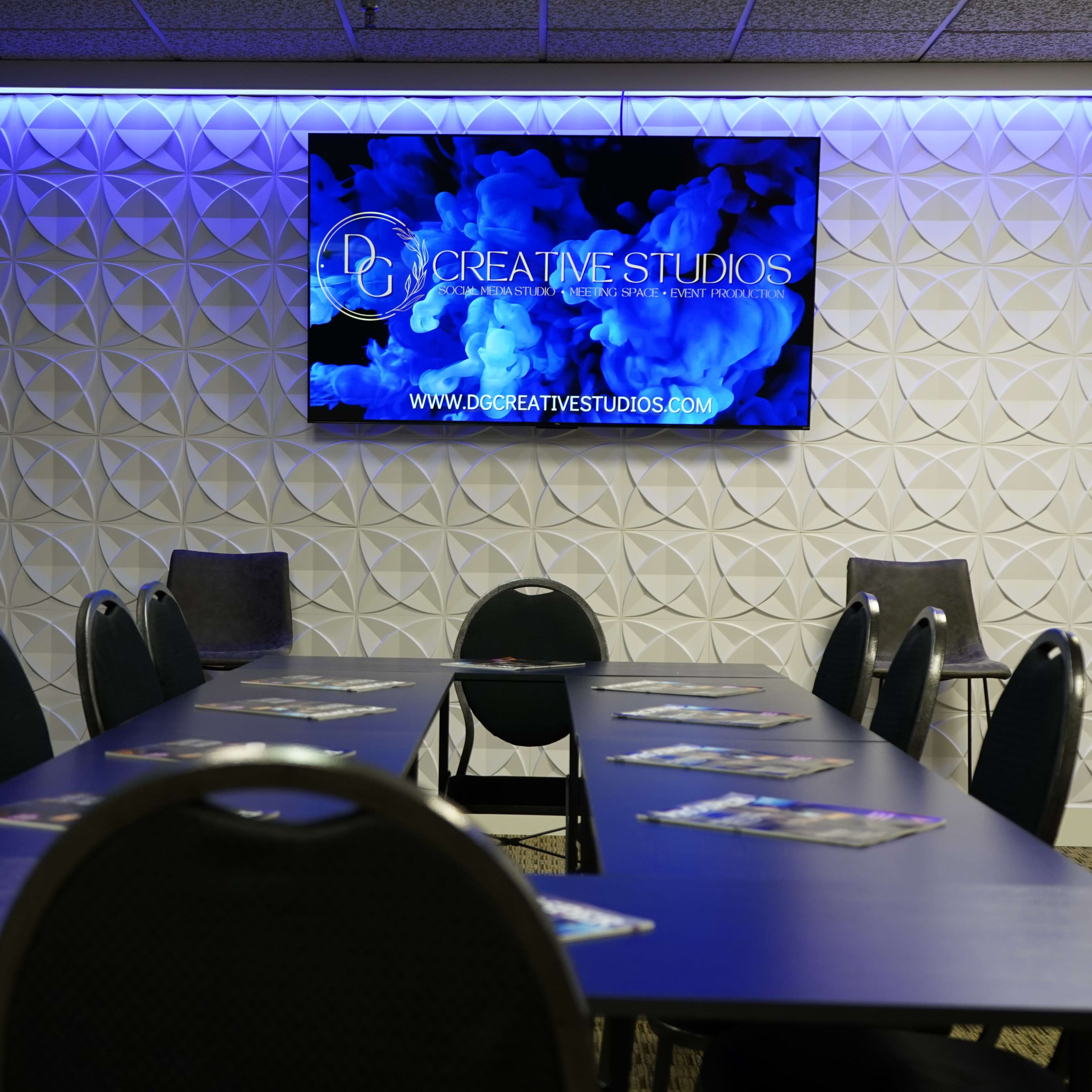 A conference room features a long table with chairs, illuminated by blue lighting, and a screen displaying the logo of D7 Creative Studios on the wall.