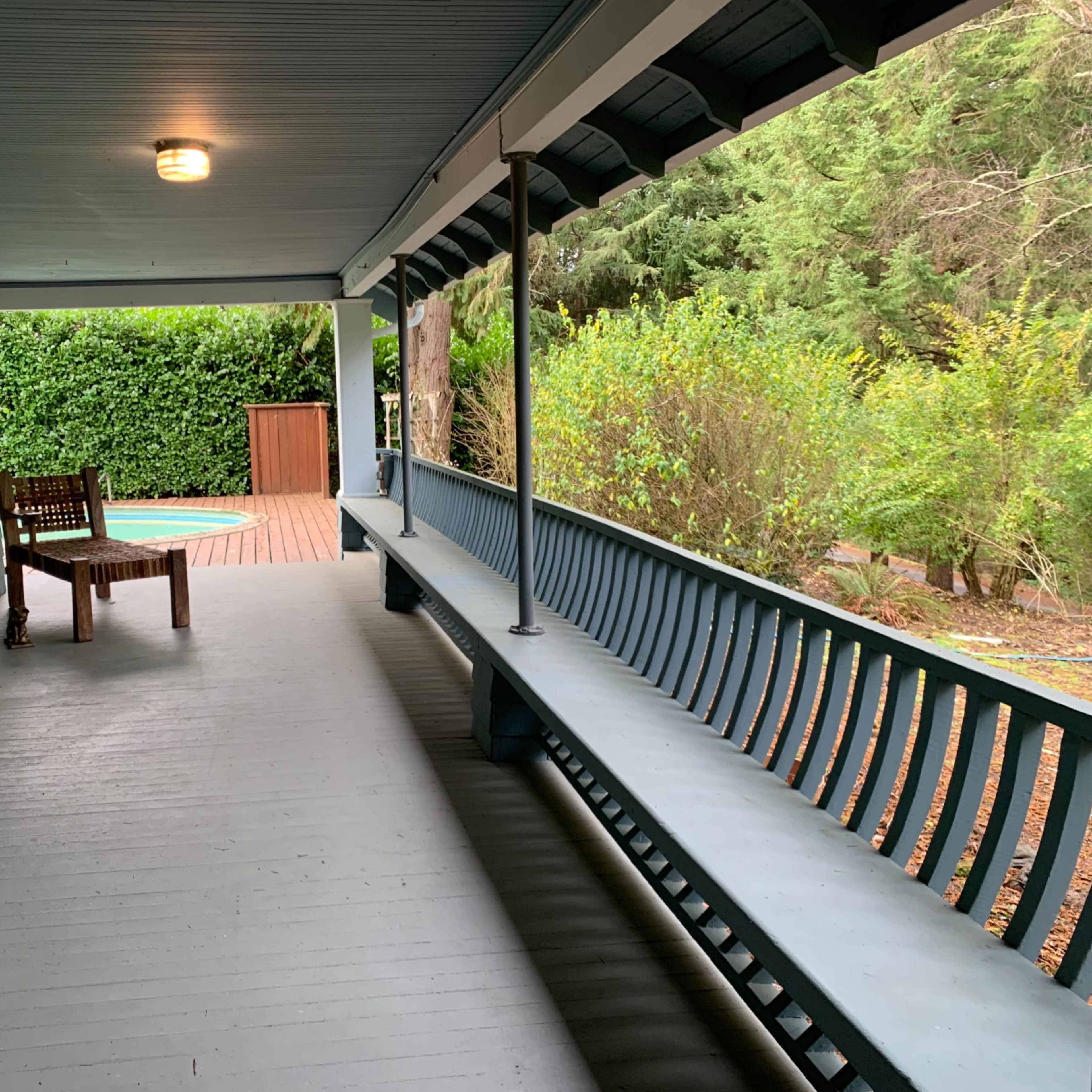 A covered porch with a wooden bench and a view of a backyard surrounded by greenery.
