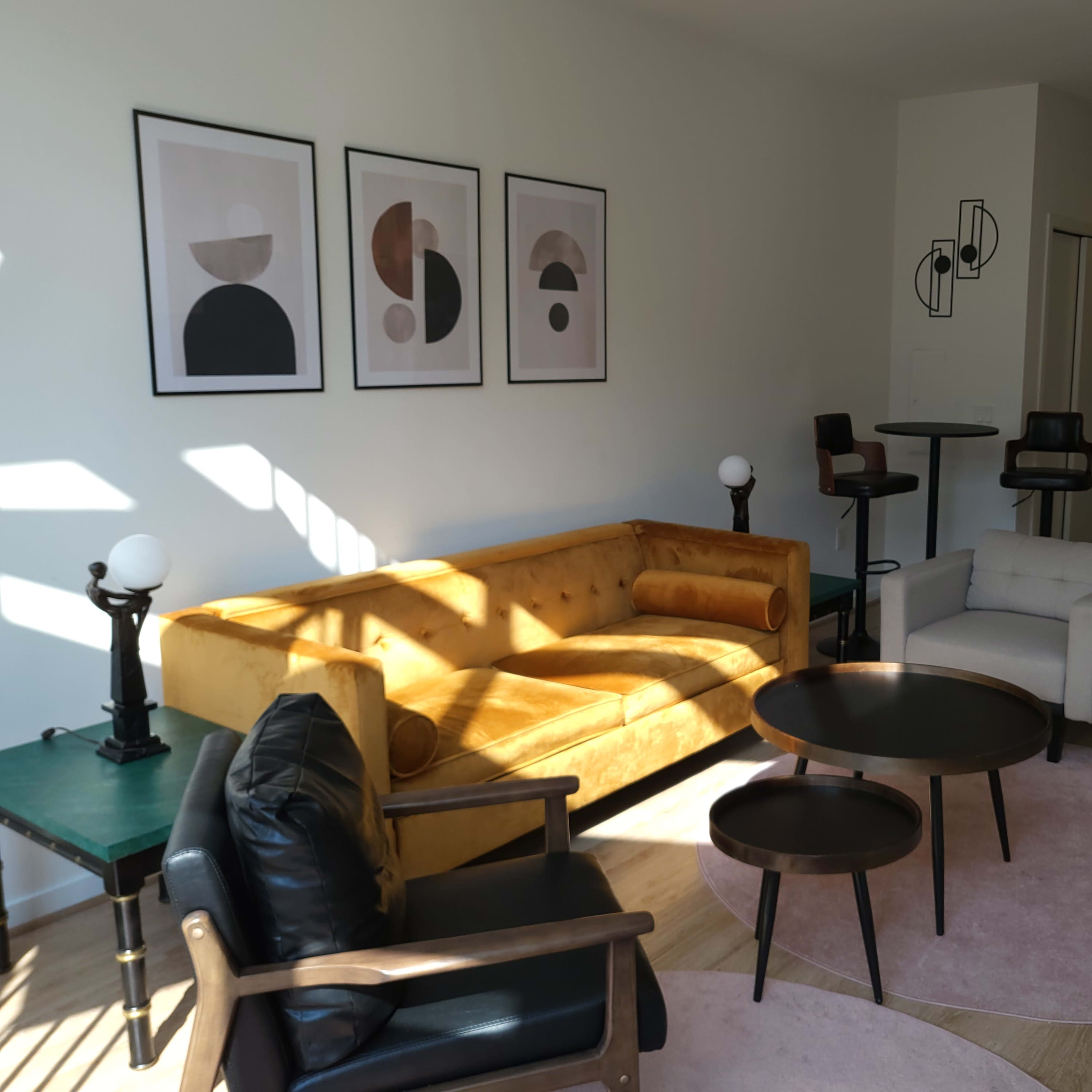 A modern living room featuring a yellow sofa, circular coffee tables, and various wall art pieces.