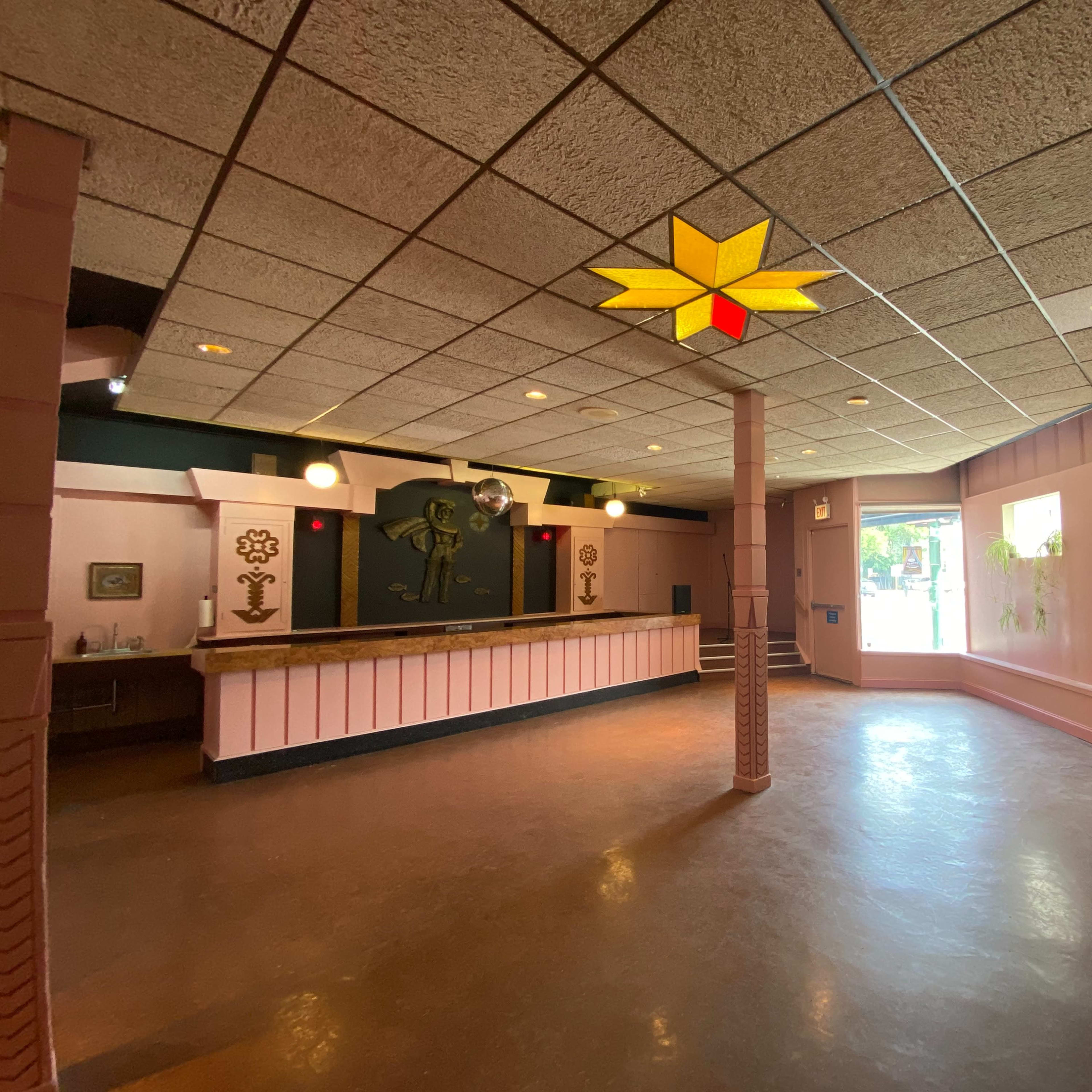 An empty room with a bar area, decorative wall features, and a large window letting in natural light.