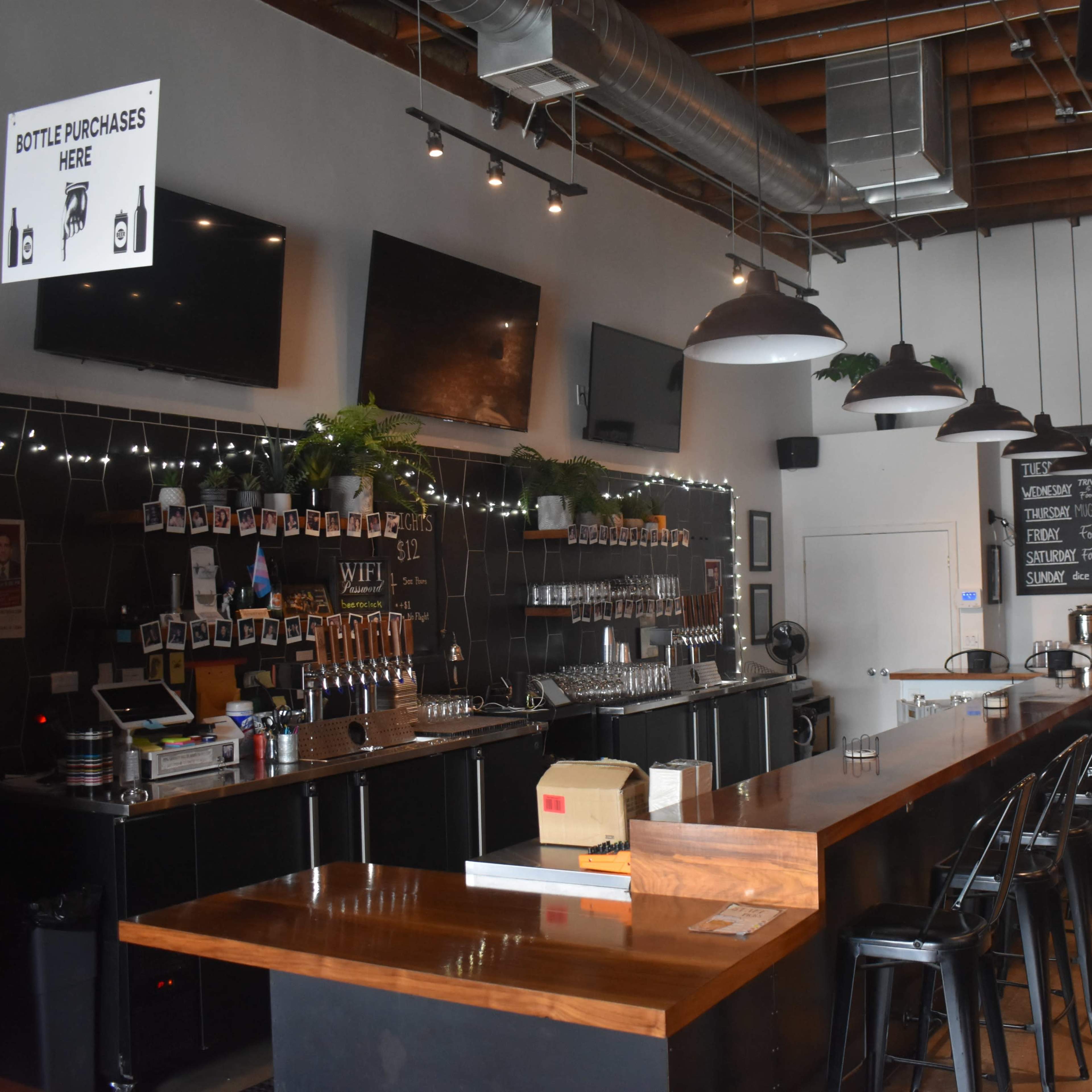 The interior of a bar with a long wooden counter, multiple seating options, and decorative lighting.