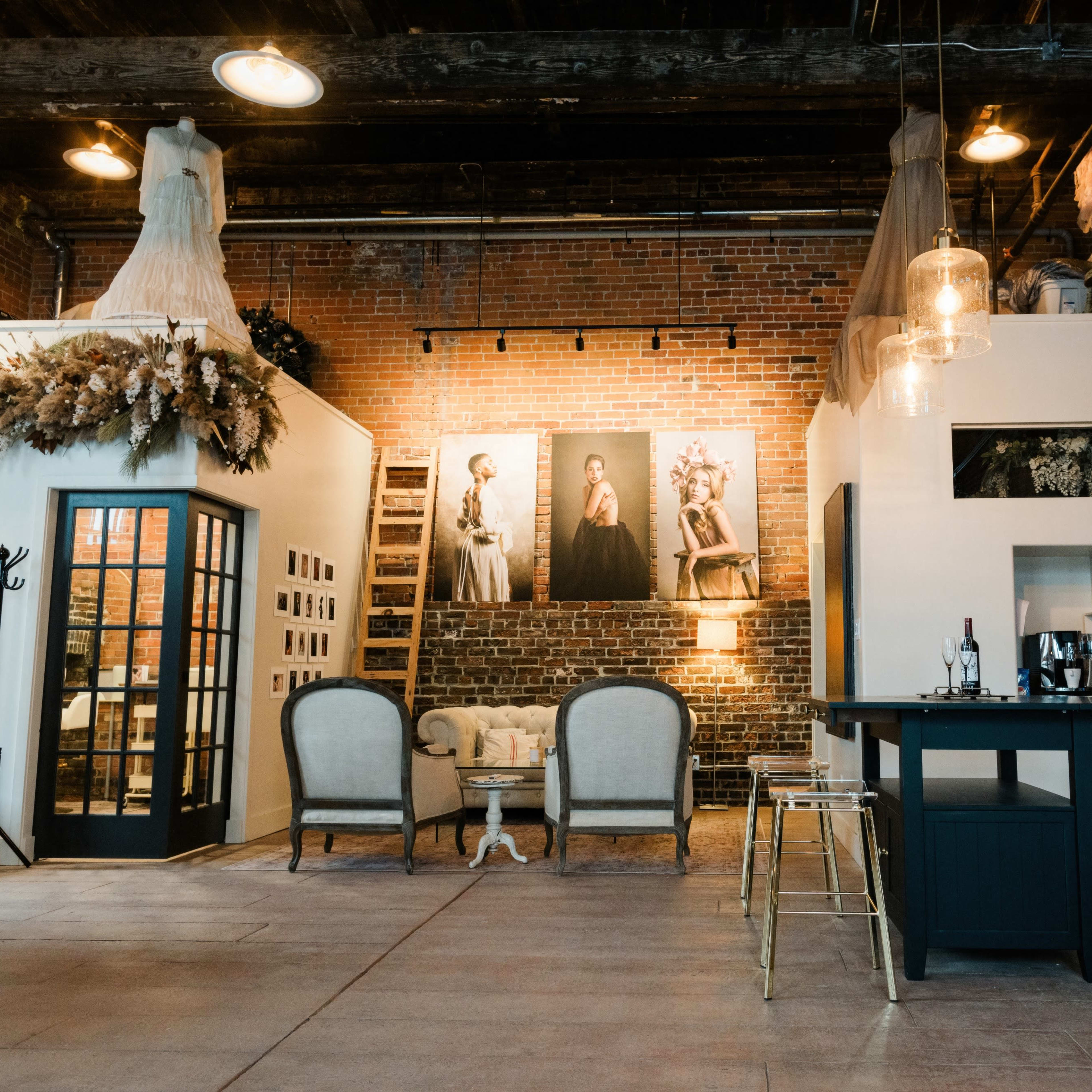 A spacious loft-style interior with exposed brick walls, a seating area, a bar-style table, and artistic photographs displayed on the walls.