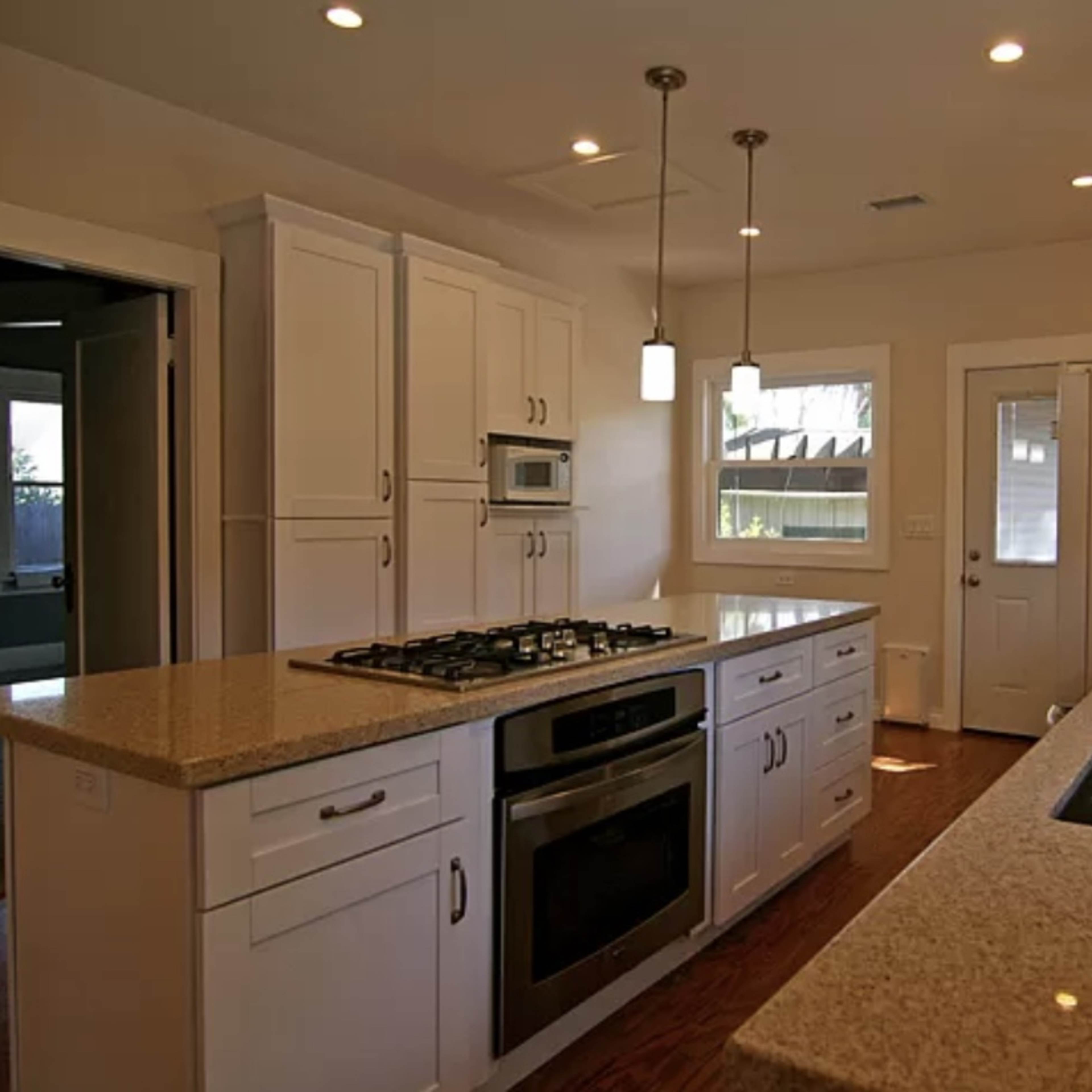 A modern kitchen features white cabinets, a gas stovetop, and a double-basin sink with granite countertops.