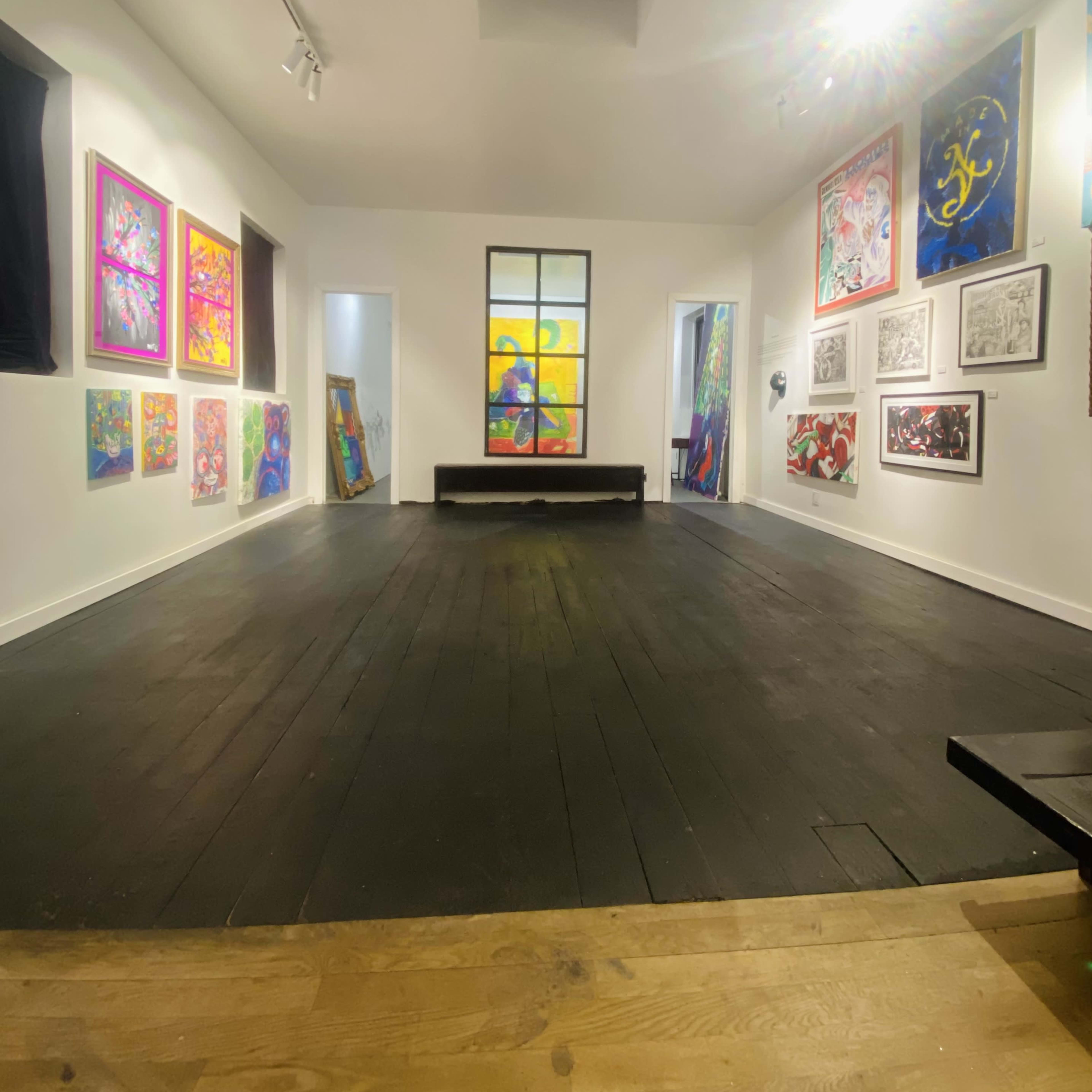 An art gallery with colorful paintings displayed on the white walls and a wooden floor.