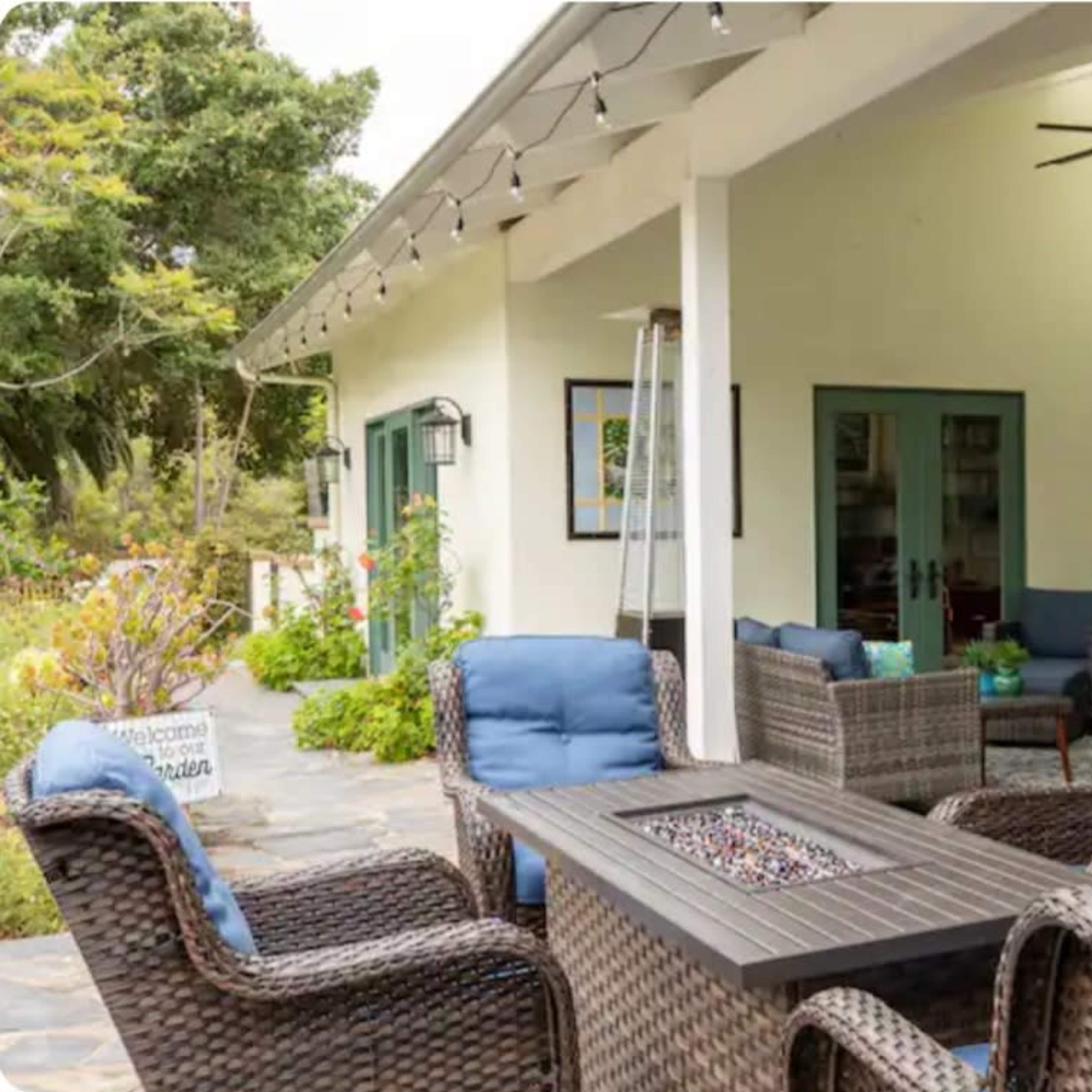 A patio area with wicker chairs and a table featuring a fire pit, alongside a wall-mounted TV.