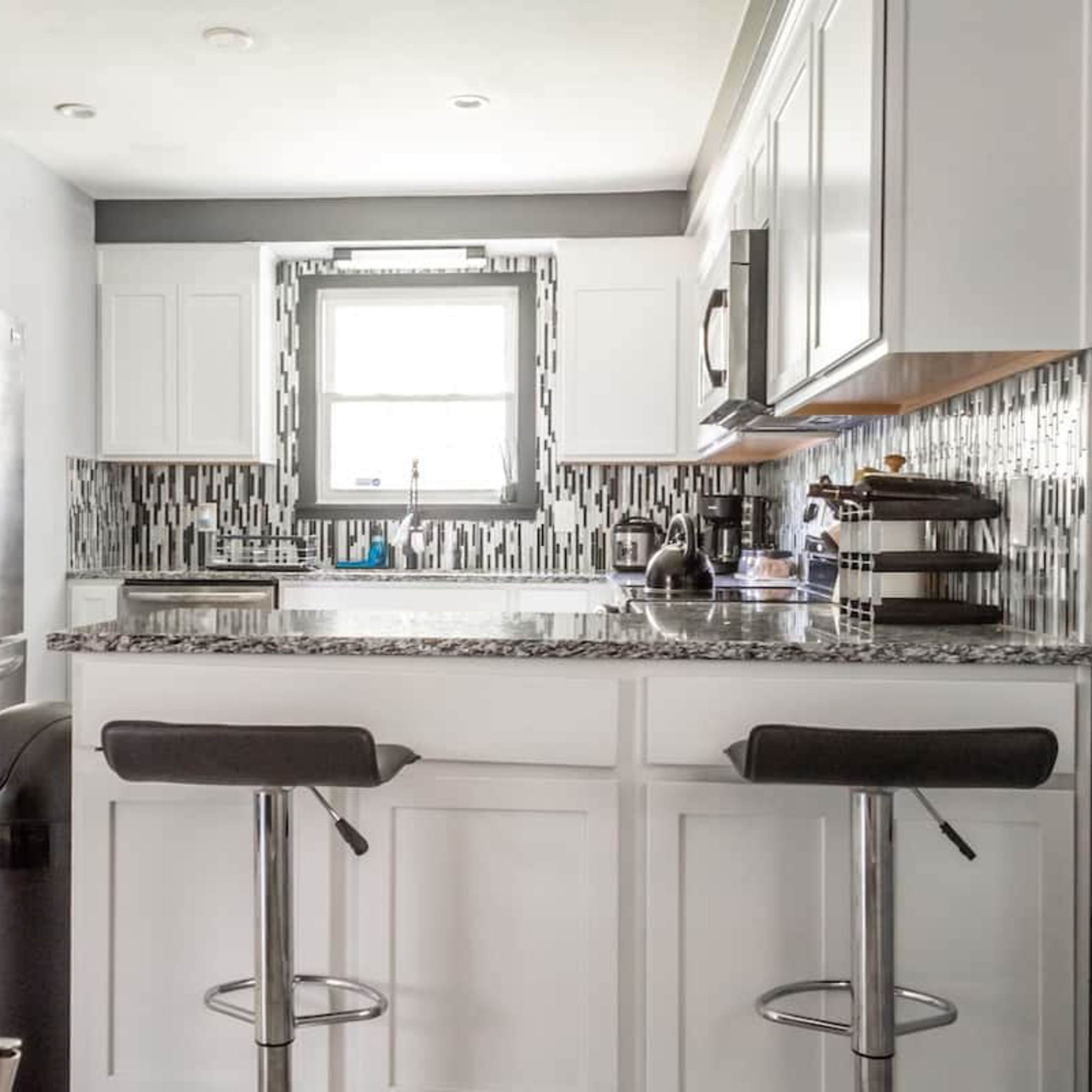 A modern kitchen features white cabinetry, a granite countertop, stainless steel appliances, and a tiled backsplash.