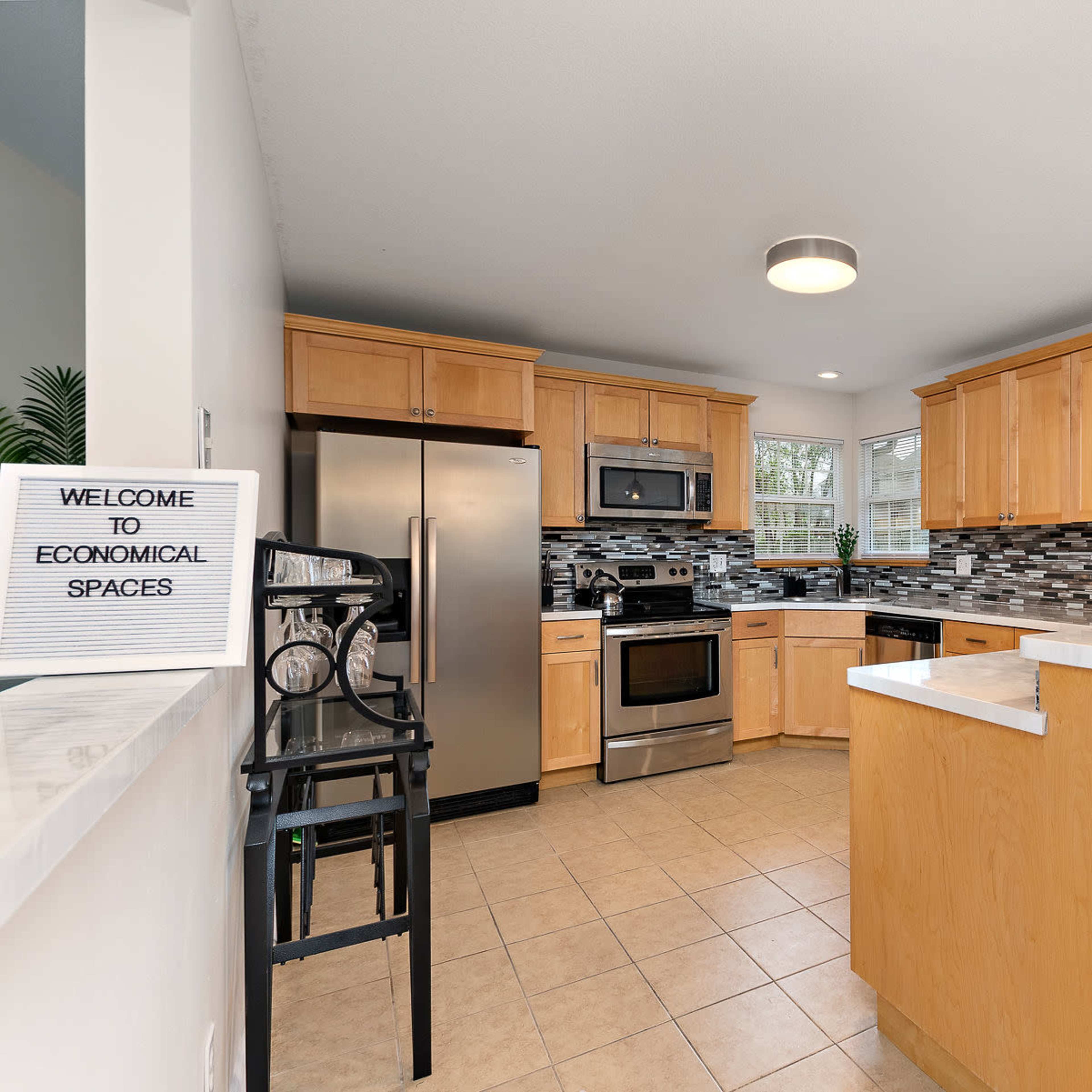 A modern kitchen with wooden cabinets, stainless steel appliances, and a counter with bar stools.
