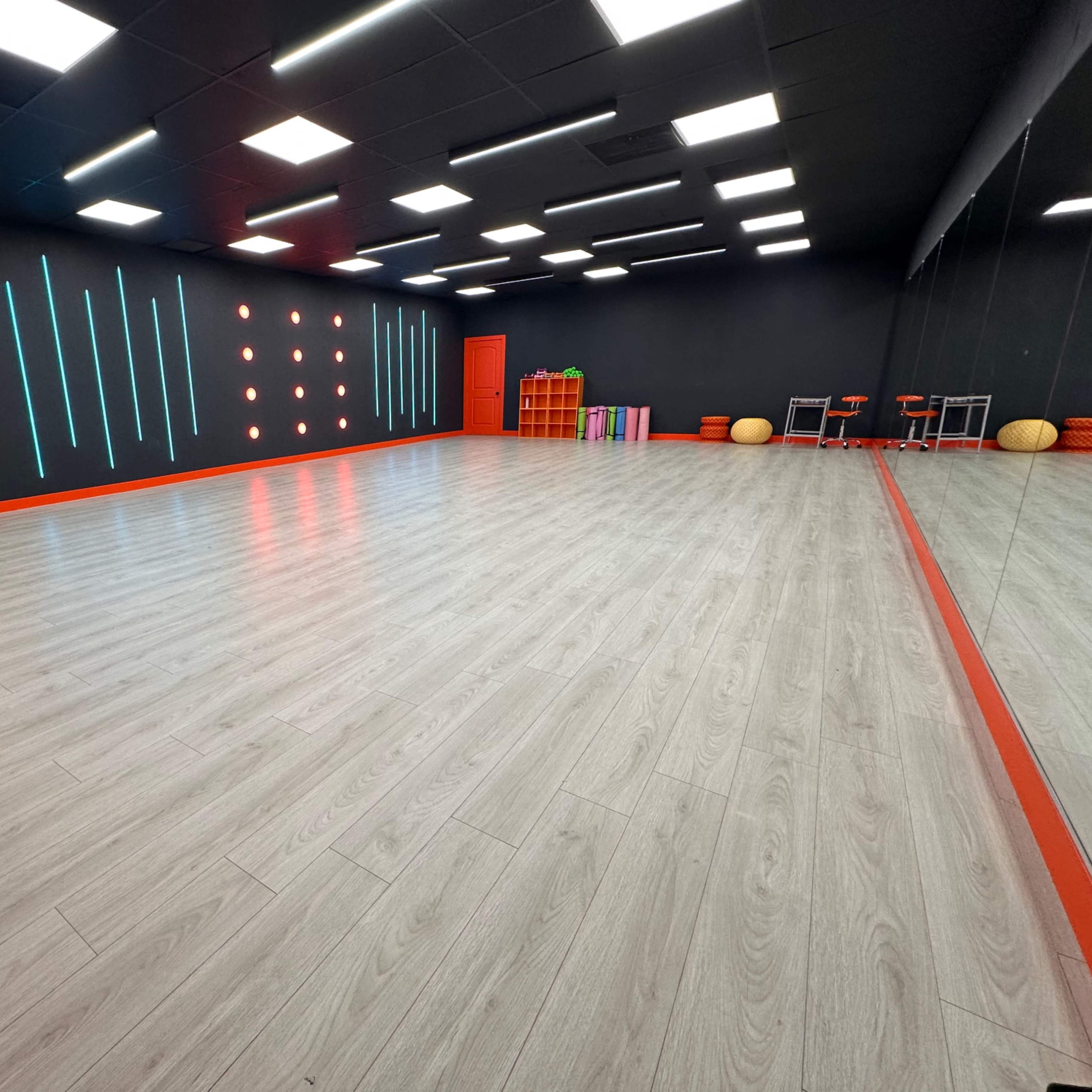 A brightly lit exercise studio with a wooden floor, black walls, and colorful accents, including a red door and vibrant wall decorations.