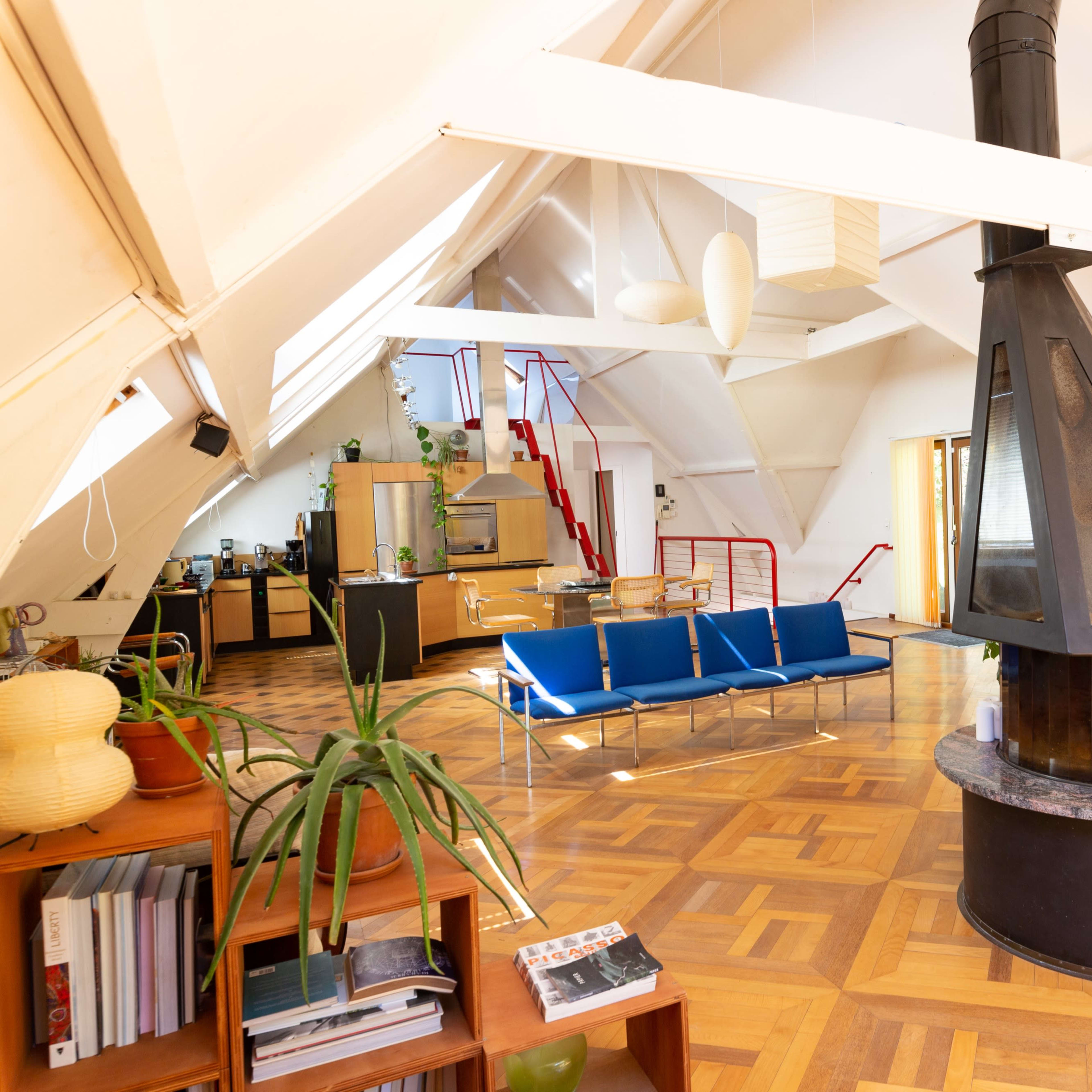 A spacious, modern living area with a central fireplace, wooden flooring, and large windows.